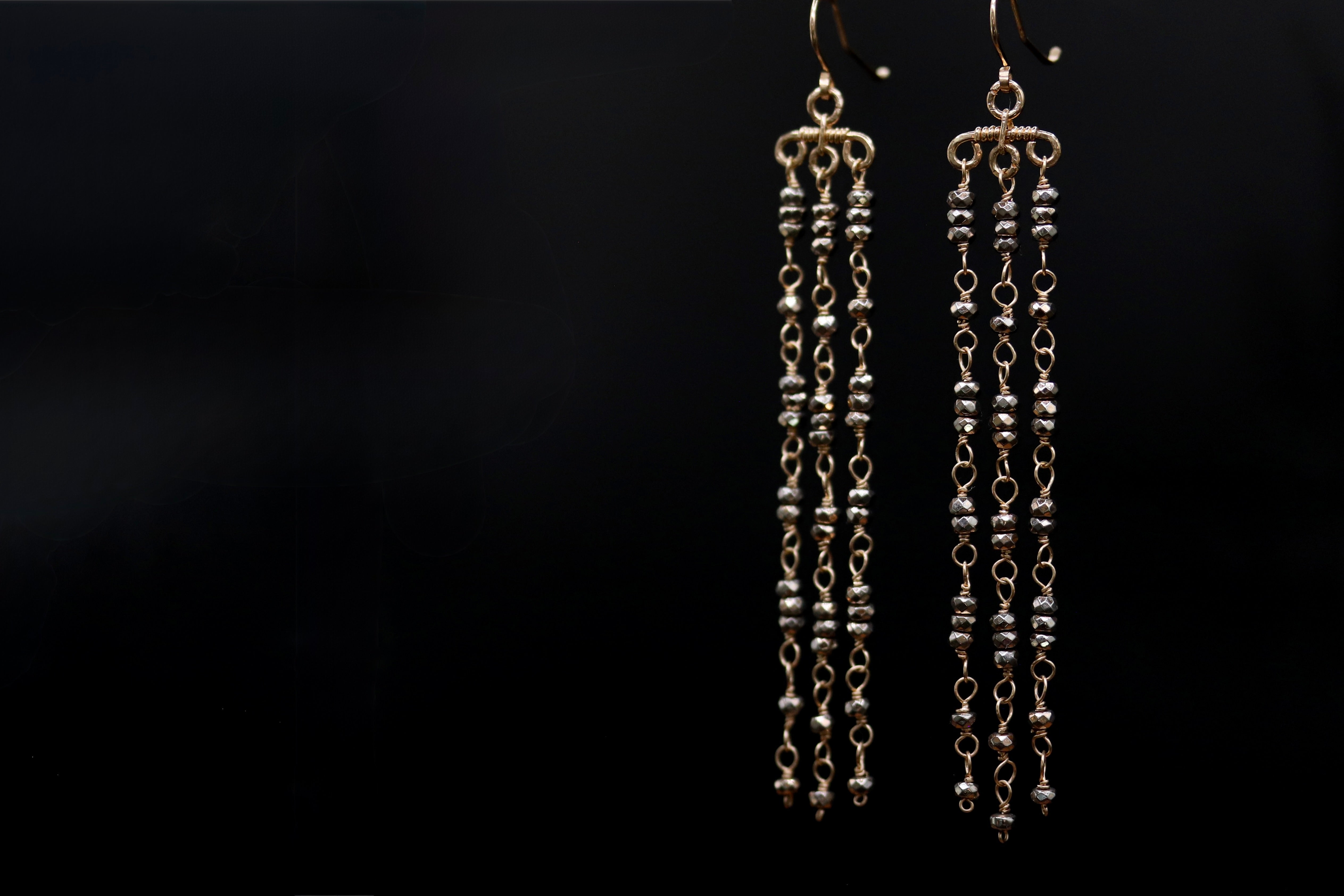 A pair of gold earrings with long, dangling chains against a dark background.