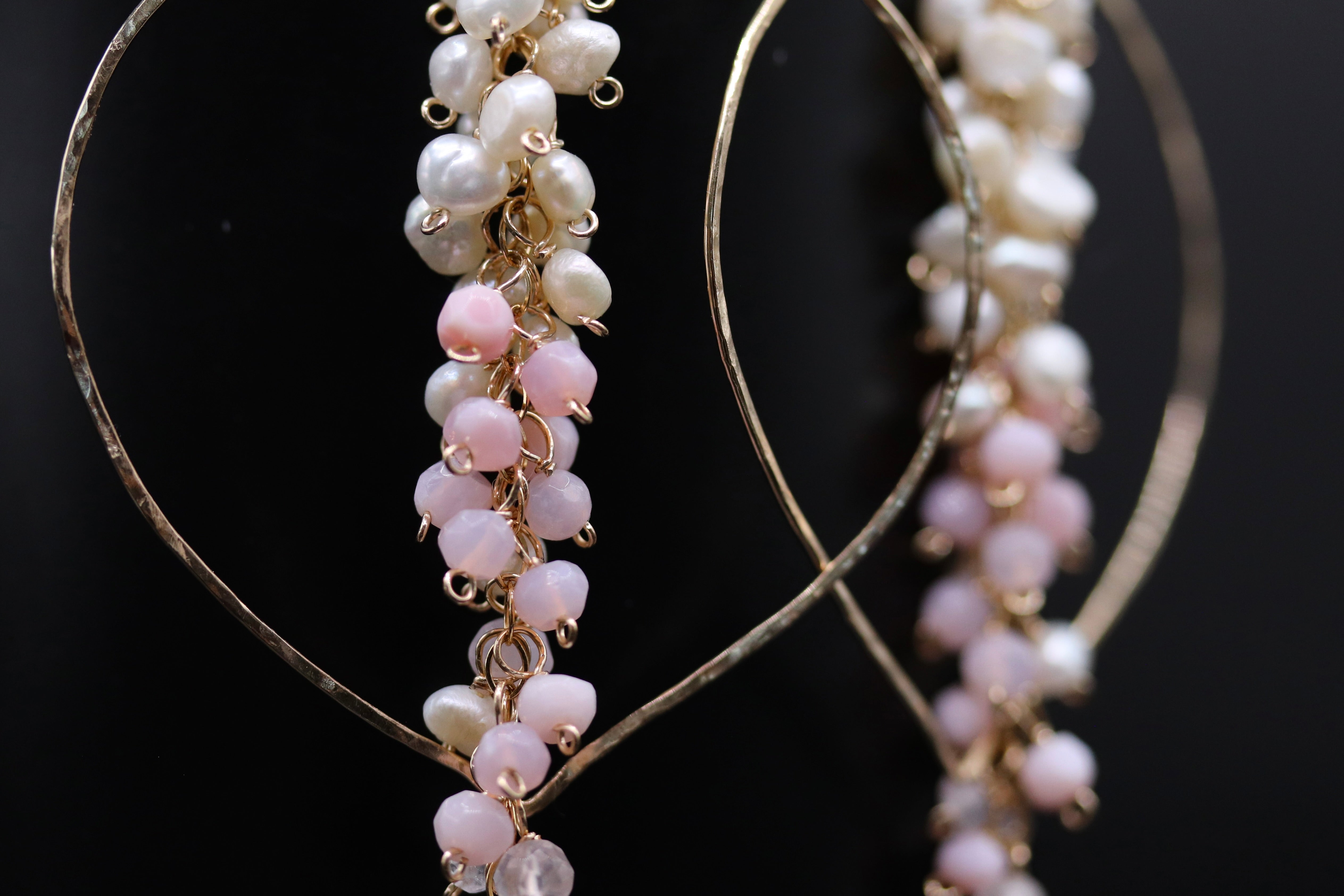 A close-up view of a pair of earrings with a combination of white and pink pearls and small beads hanging from the earrings.