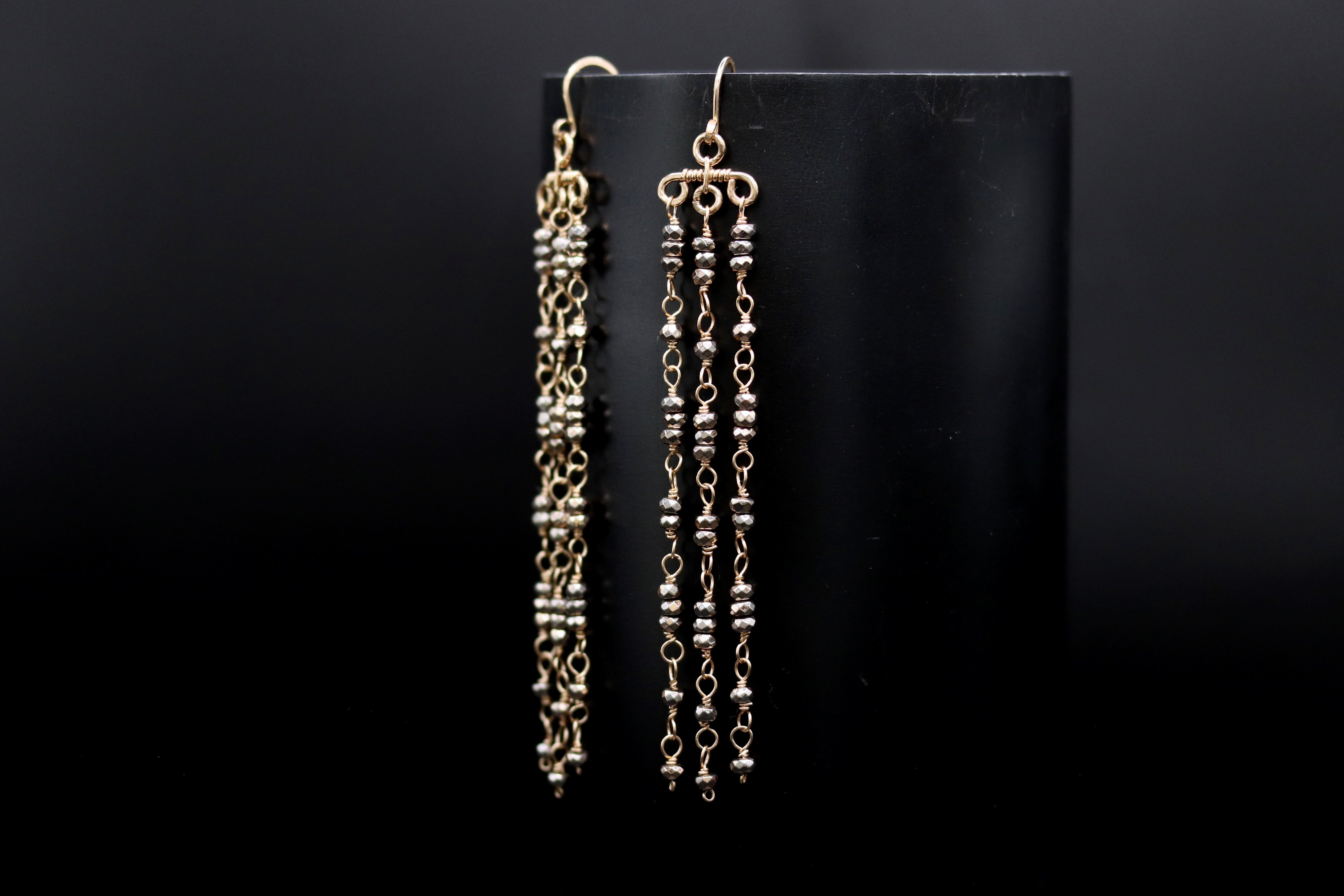 A pair of gold earrings with long, dangling chains and small beads hanging from them, displayed against a black background.