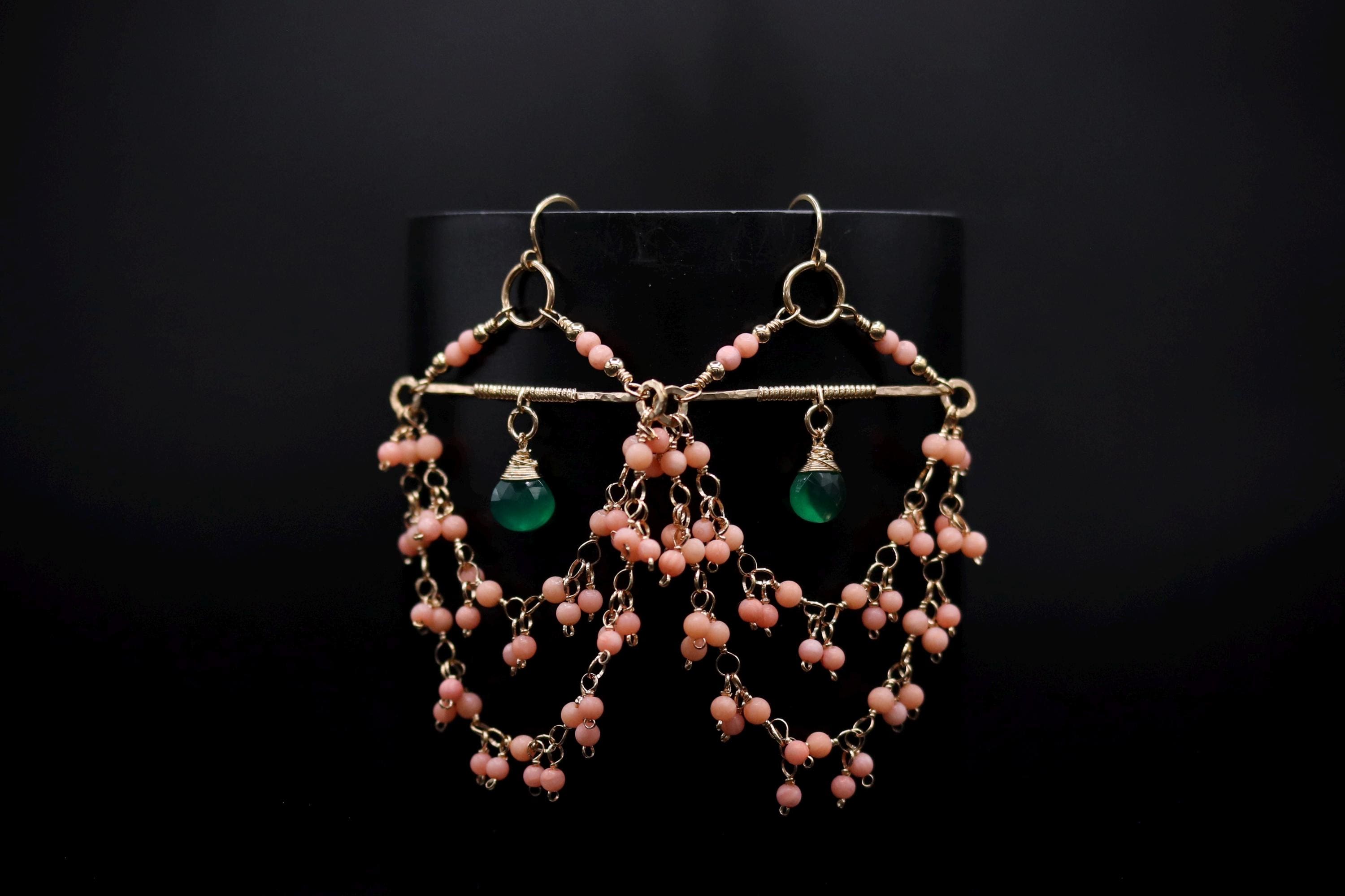 A pair of earrings with a black background and a gold frame, featuring a combination of pink and green beads.