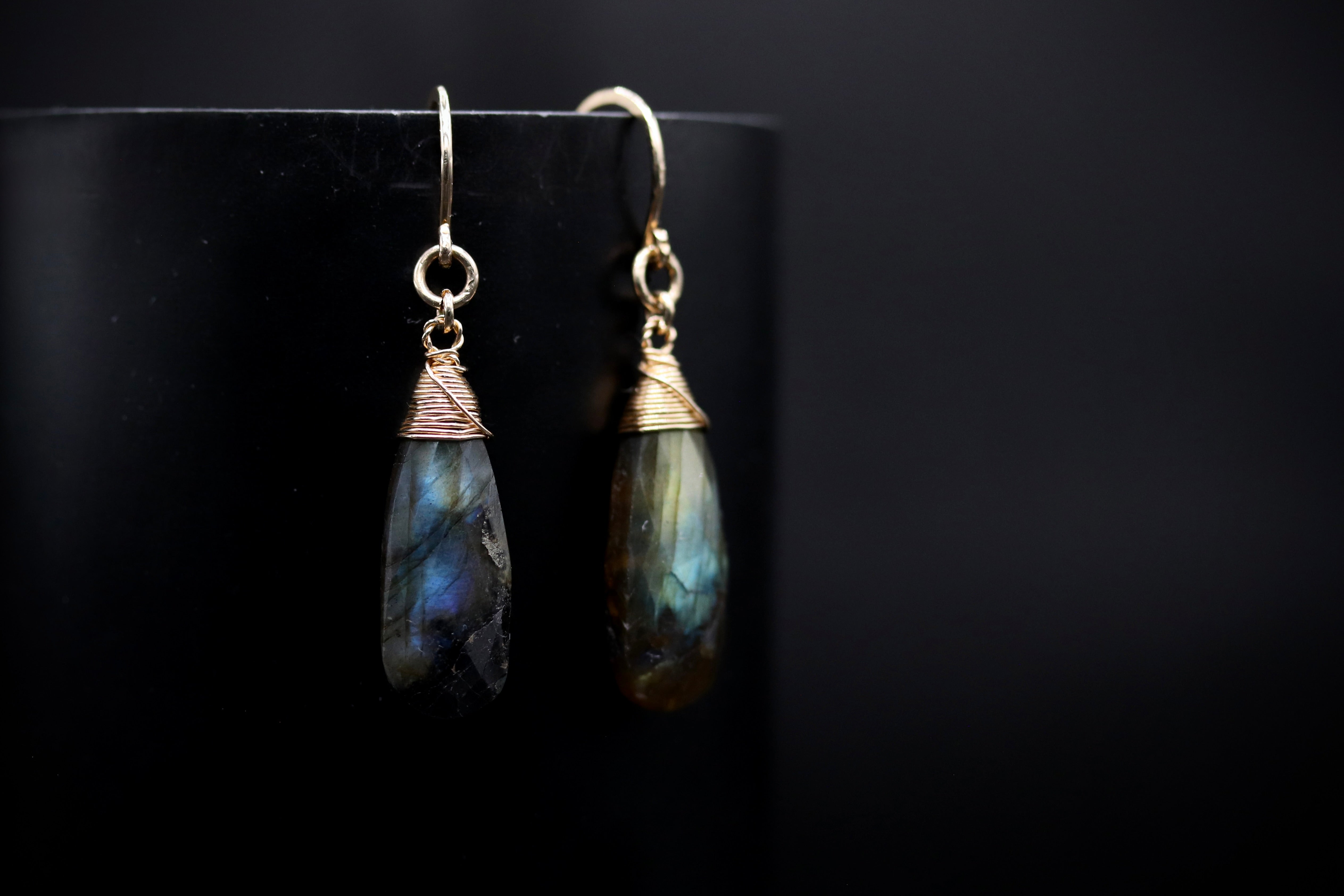 A pair of elegant earrings with a dark blue and green stone pendant, displayed against a black background.