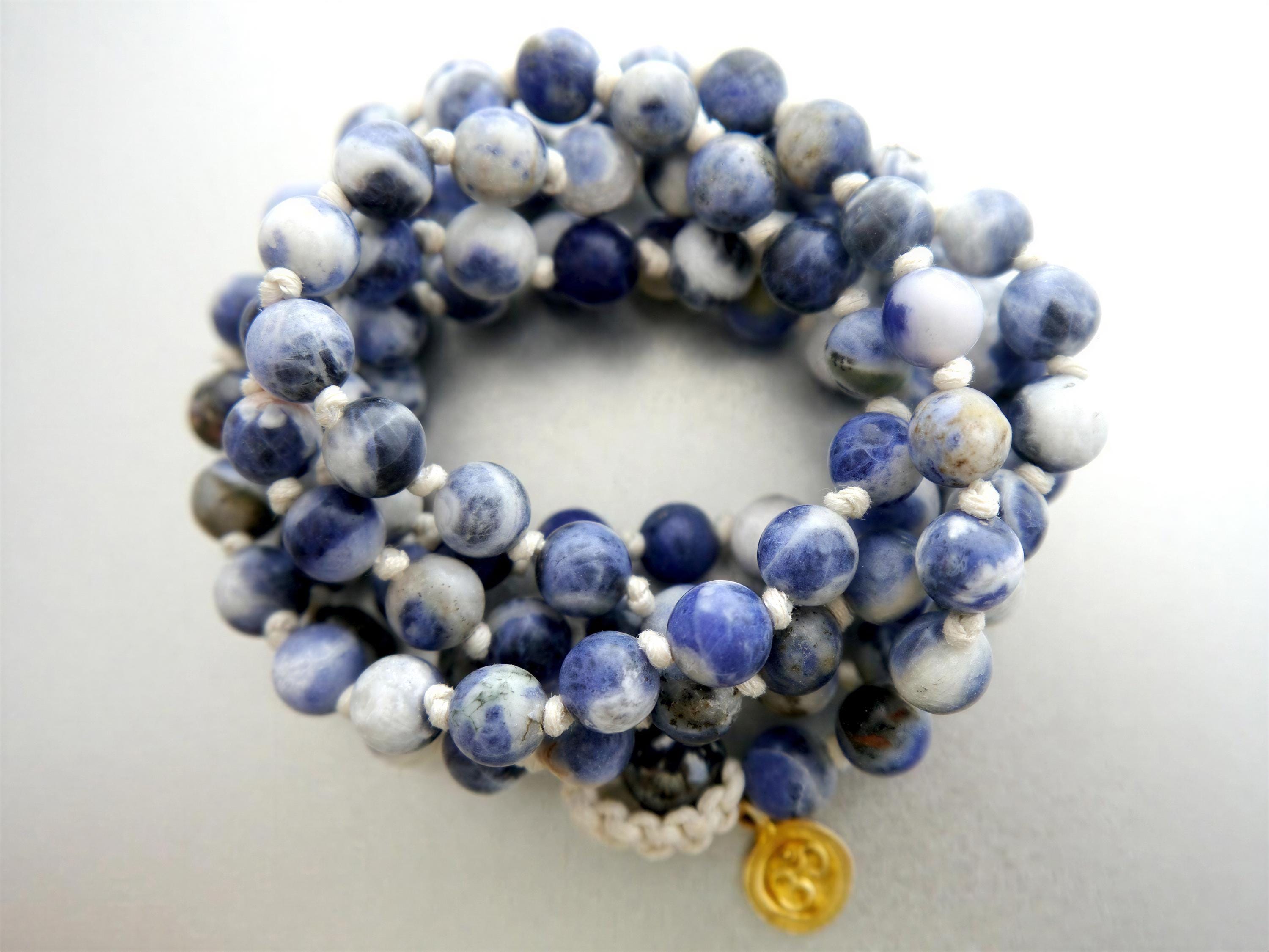 A close-up image of a bracelet composed of numerous blue and white beads, with a gold charm attached.