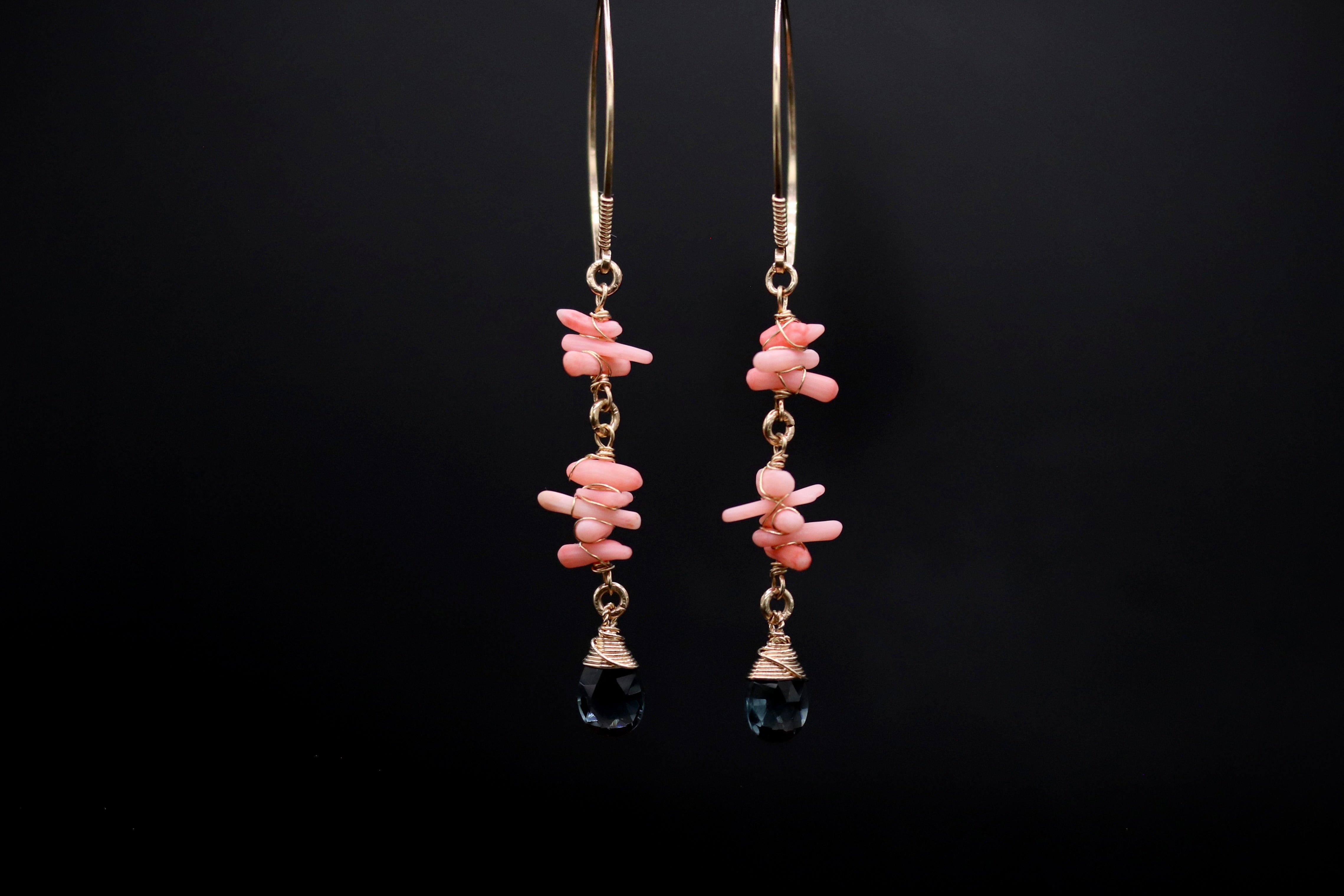 A pair of earrings with a combination of pink and black stones, hanging from gold hooks against a black background.