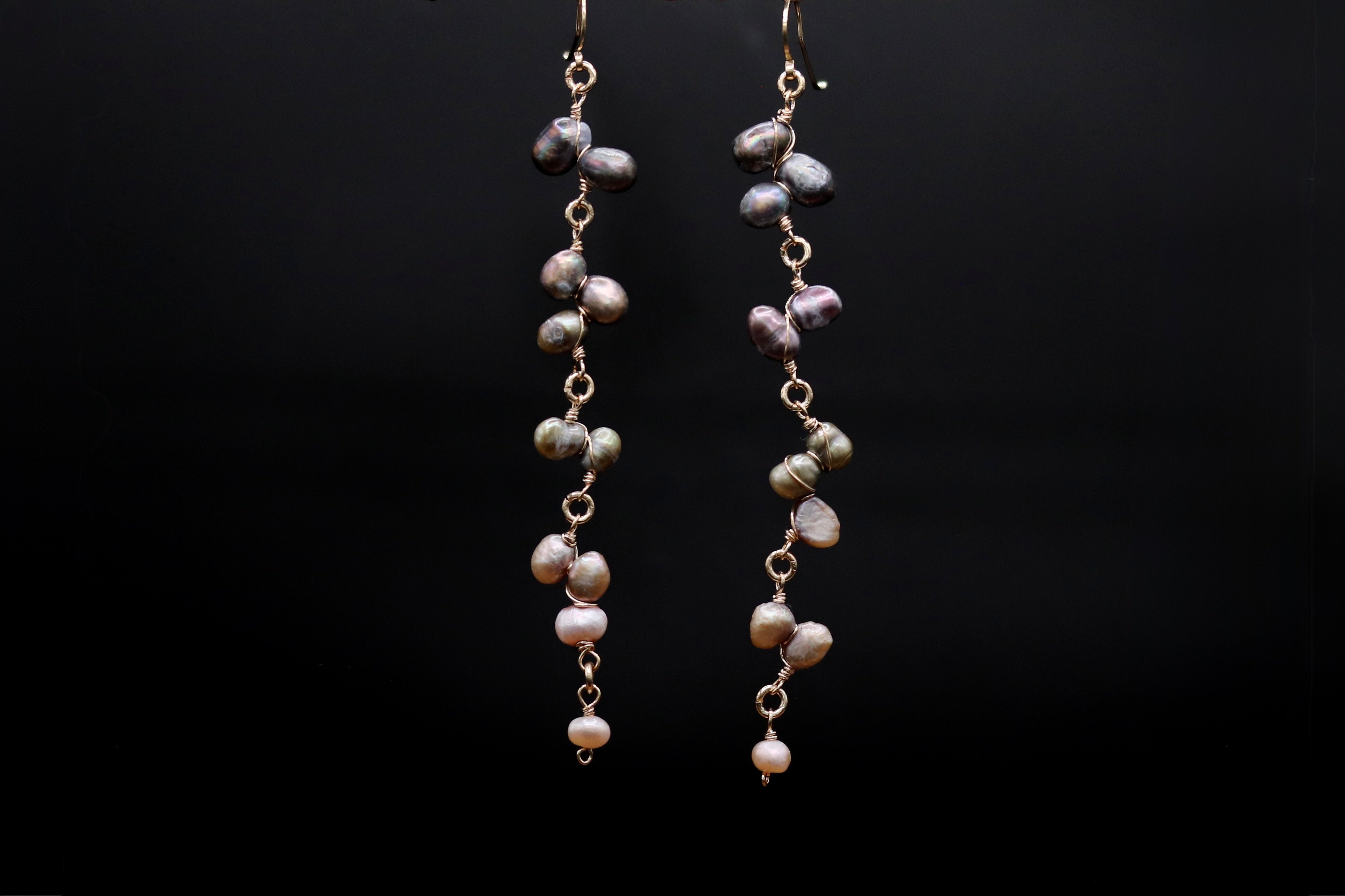 A pair of earrings with a long chain and small, round beads hanging from it, set against a black background.