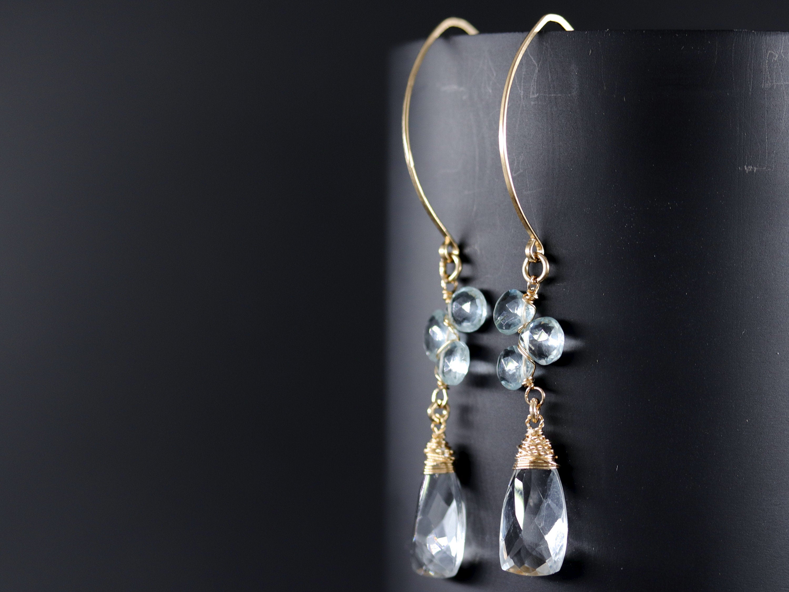 May include: Gold dangle earrings with a cluster of light blue aquamarine stones and a larger teardrop-shaped aquamarine stone hanging from each earring.