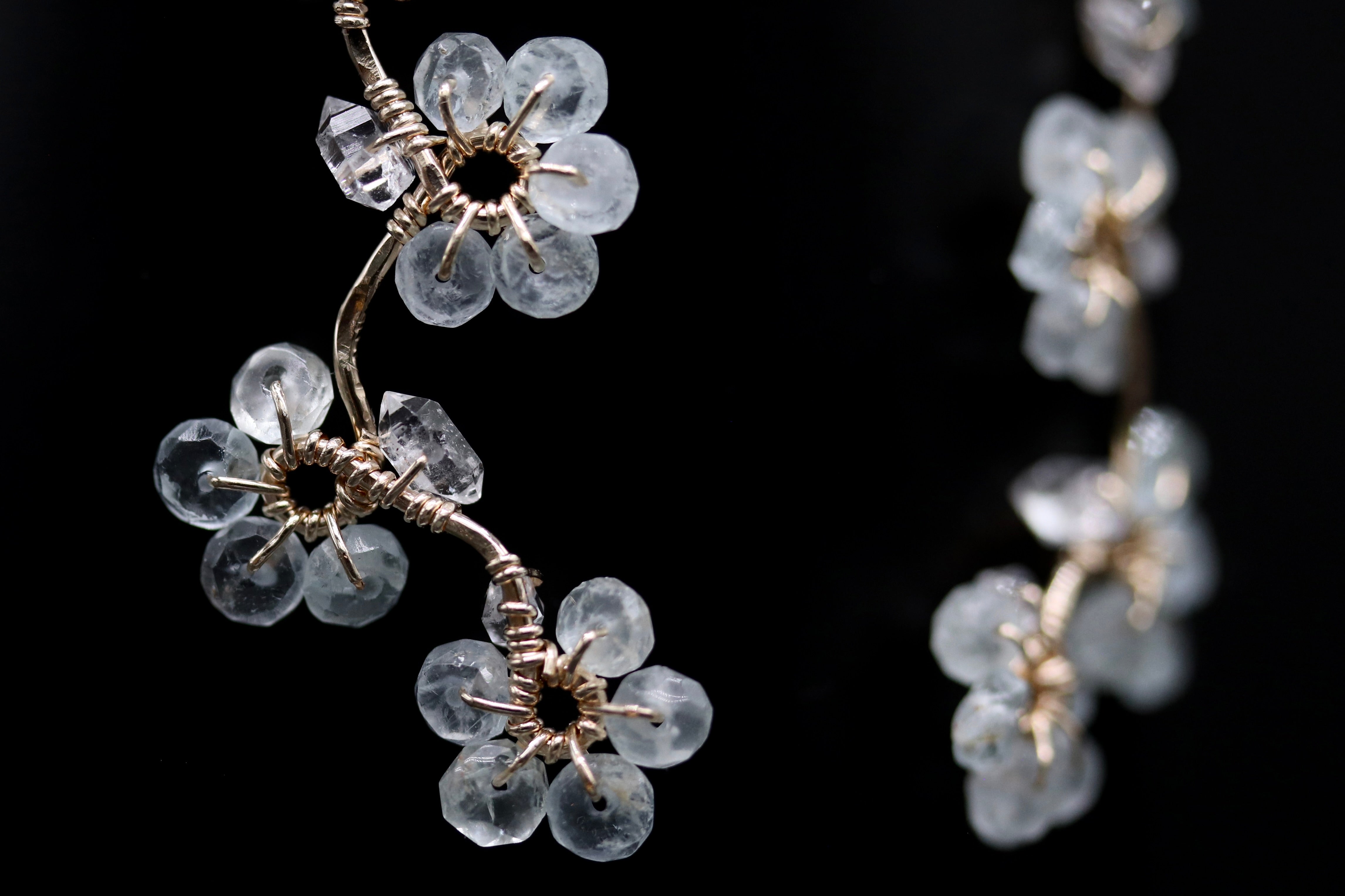 A close-up view of a delicate, intricate piece of jewelry featuring small, clear crystal flowers or branches attached to a metallic wire.