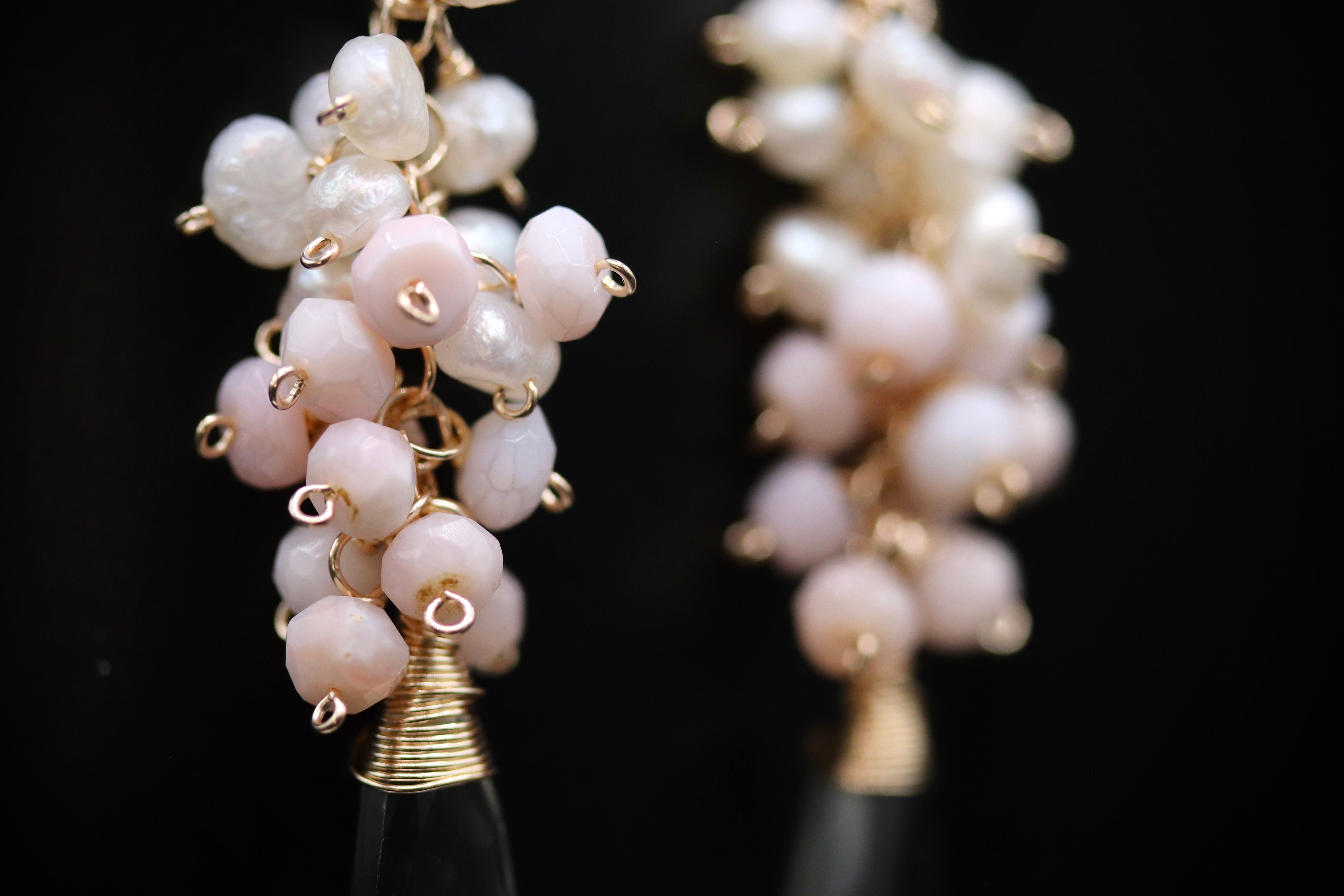 A close-up view of a pair of earrings with white and pink beads, each adorned with a gold-colored metal hook.