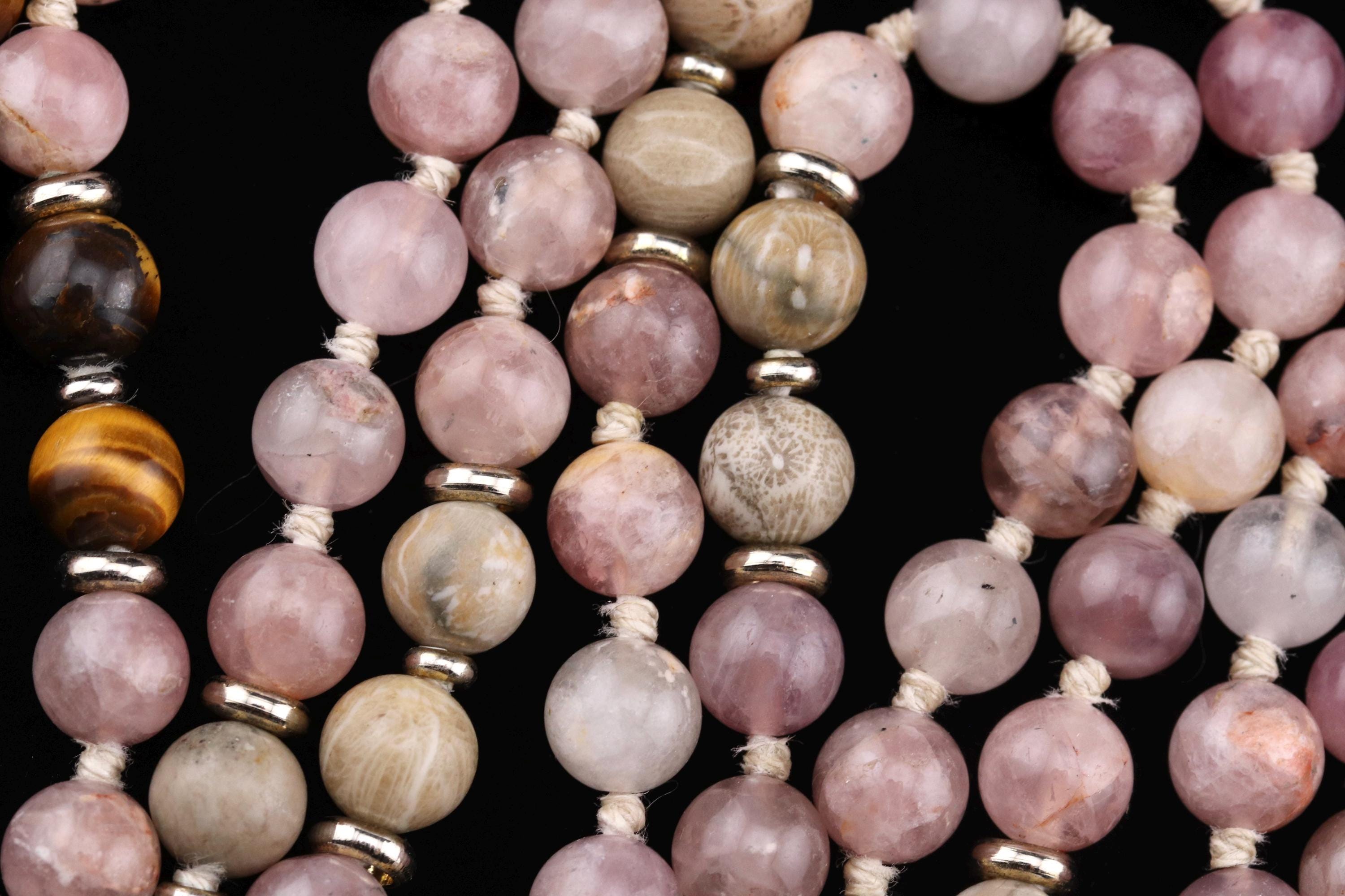 A close-up image of a collection of colorful beads, including pink, white, and brown stones, arranged in a pattern.