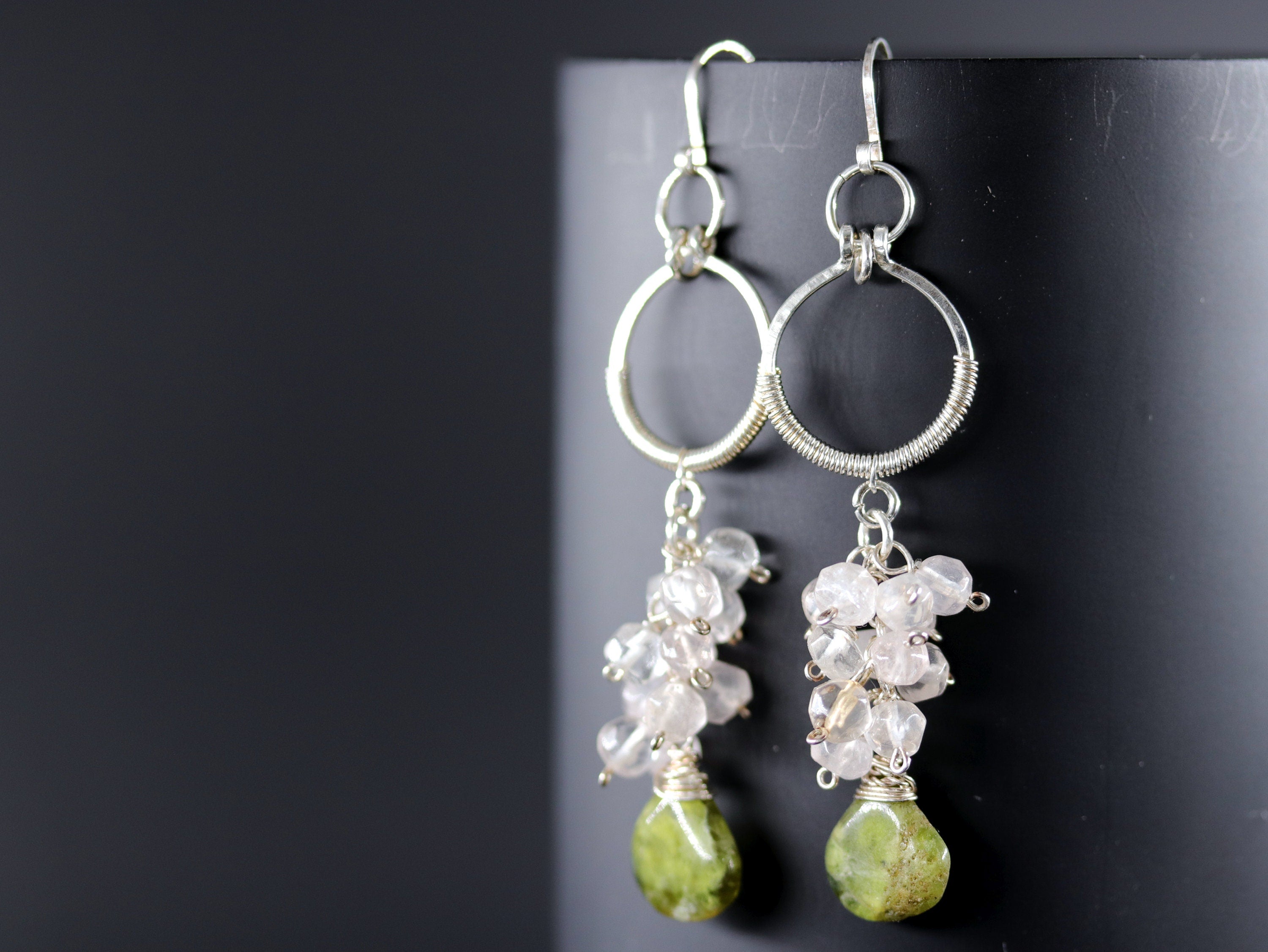 May include: Silver hoop earrings with a cluster of small pink and white stones and a larger green stone dangling from each hoop.