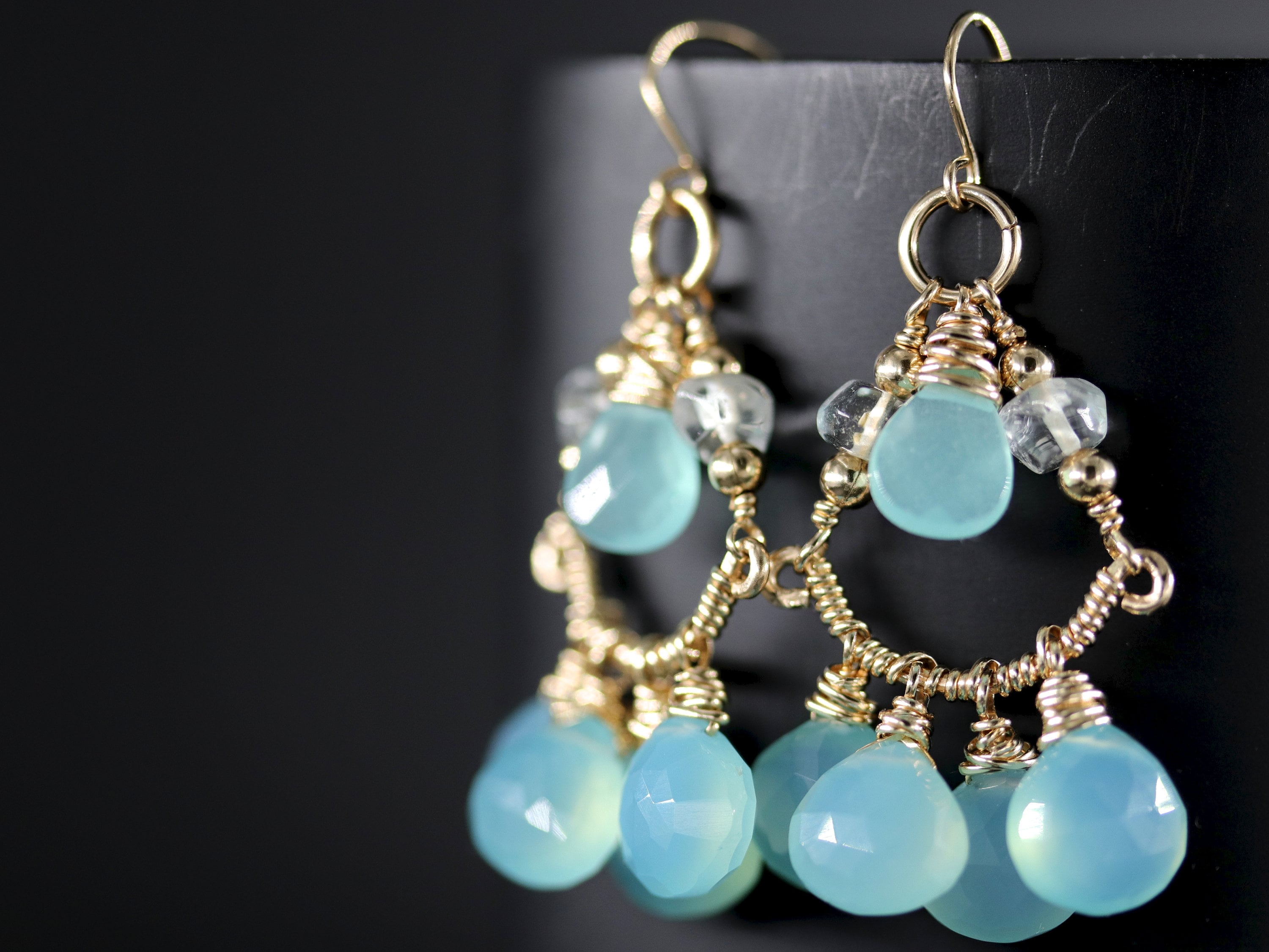 May include: Gold earrings with a teardrop-shaped blue chalcedony gemstone and clear quartz accents.