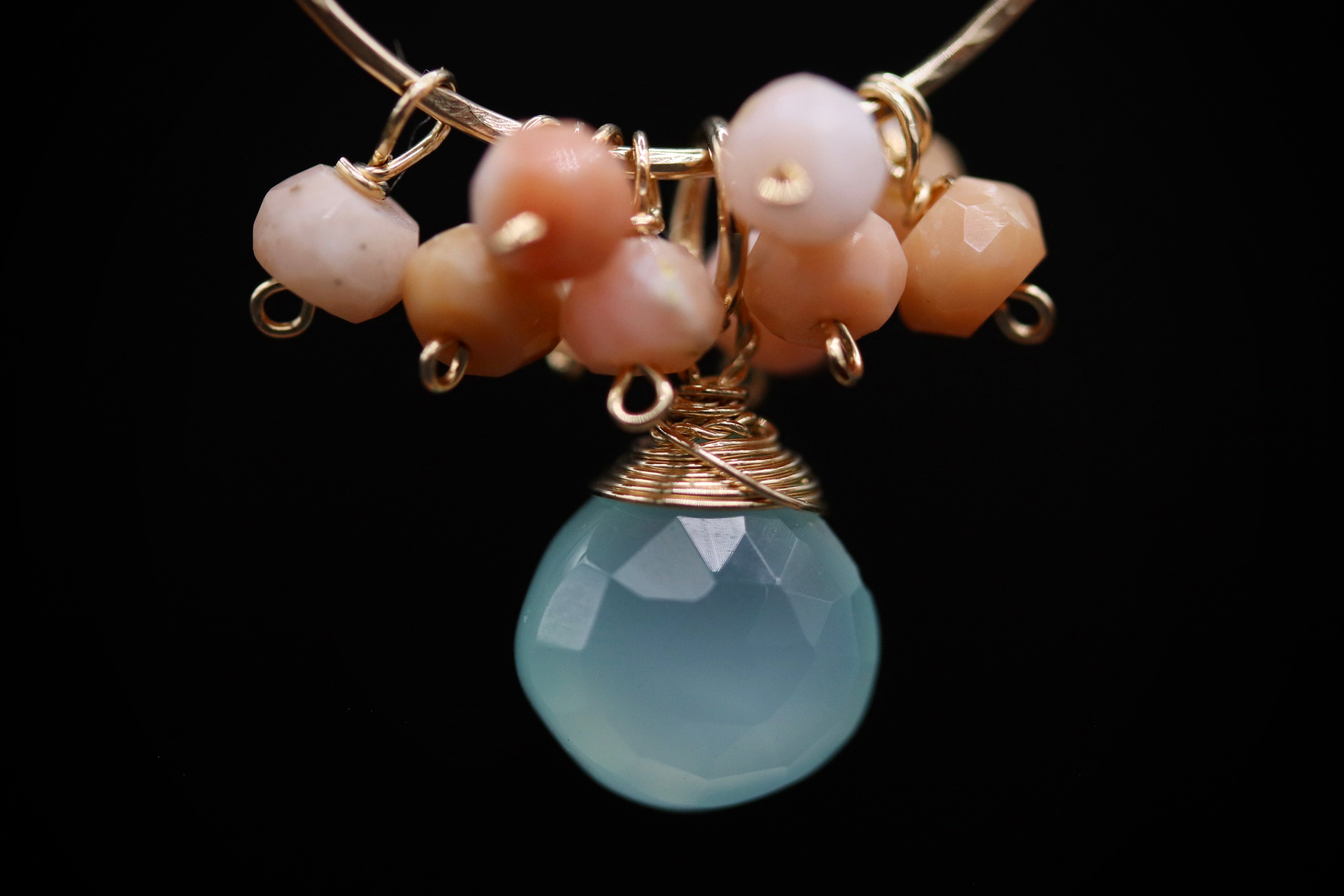 A close-up image of a necklace with a large, round, blue stone pendant and a cluster of smaller, multicolored beads hanging from a gold-colored metal clasp.