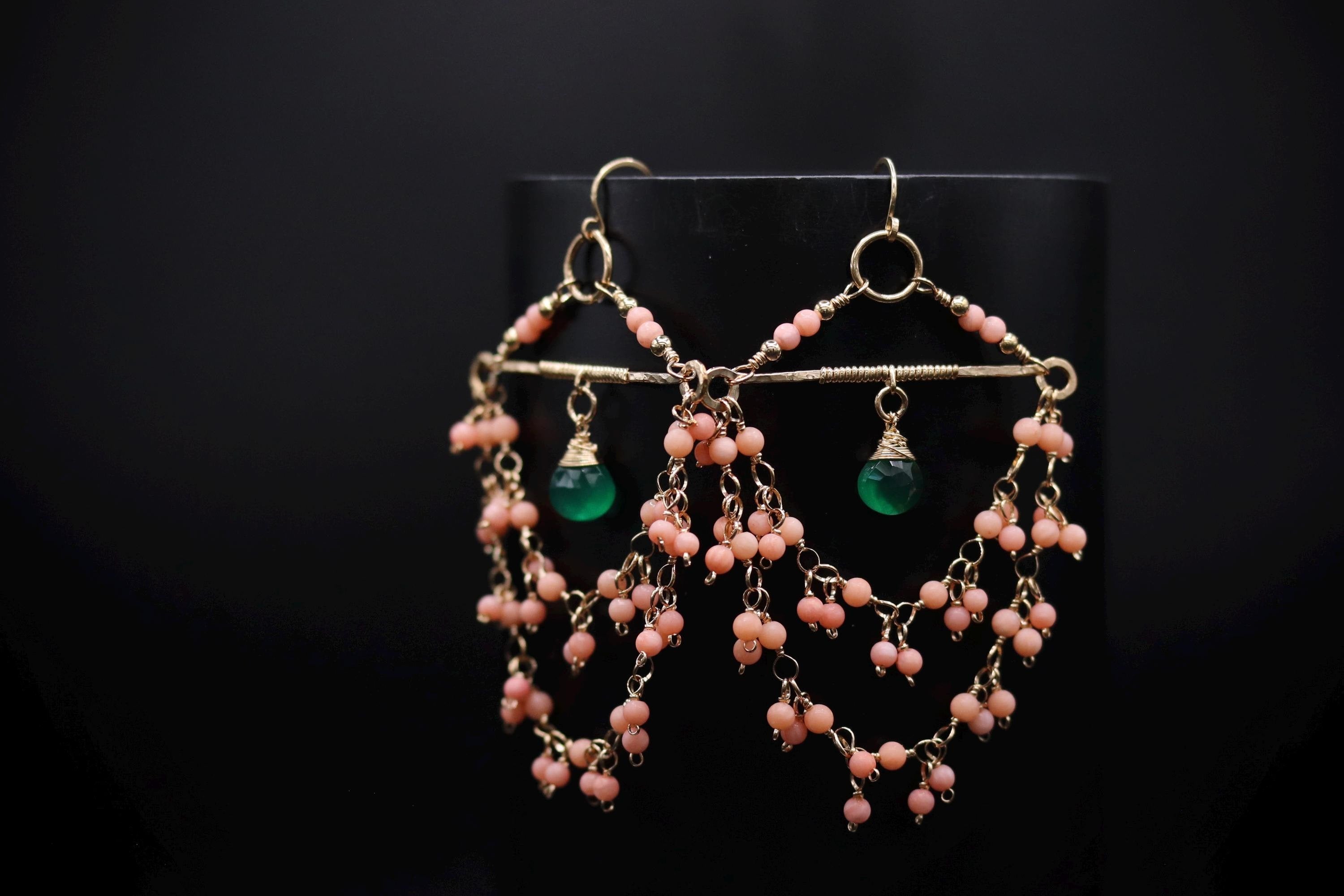 A pair of earrings with a black background and a gold frame, featuring a combination of pink and green beads.