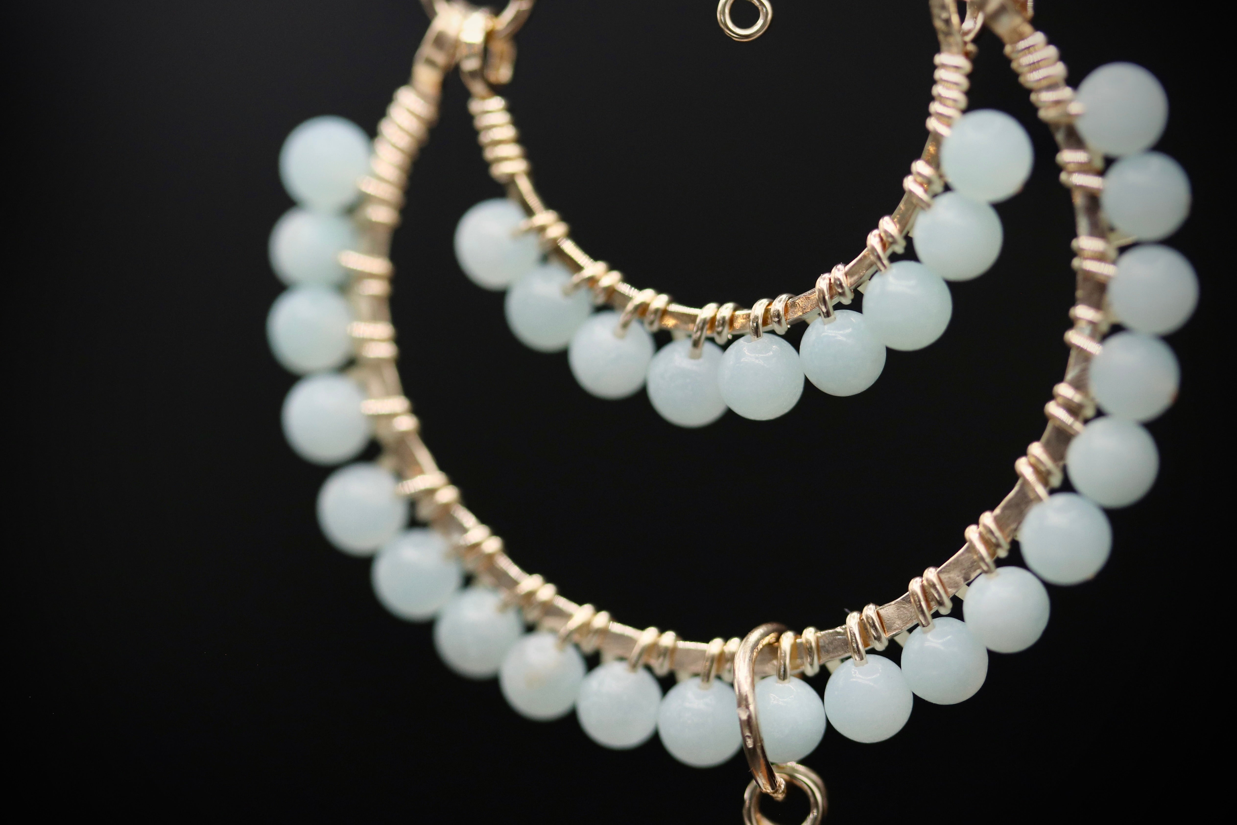 A close-up view of a delicate necklace with a series of small, round beads in a light blue color, set against a dark background.