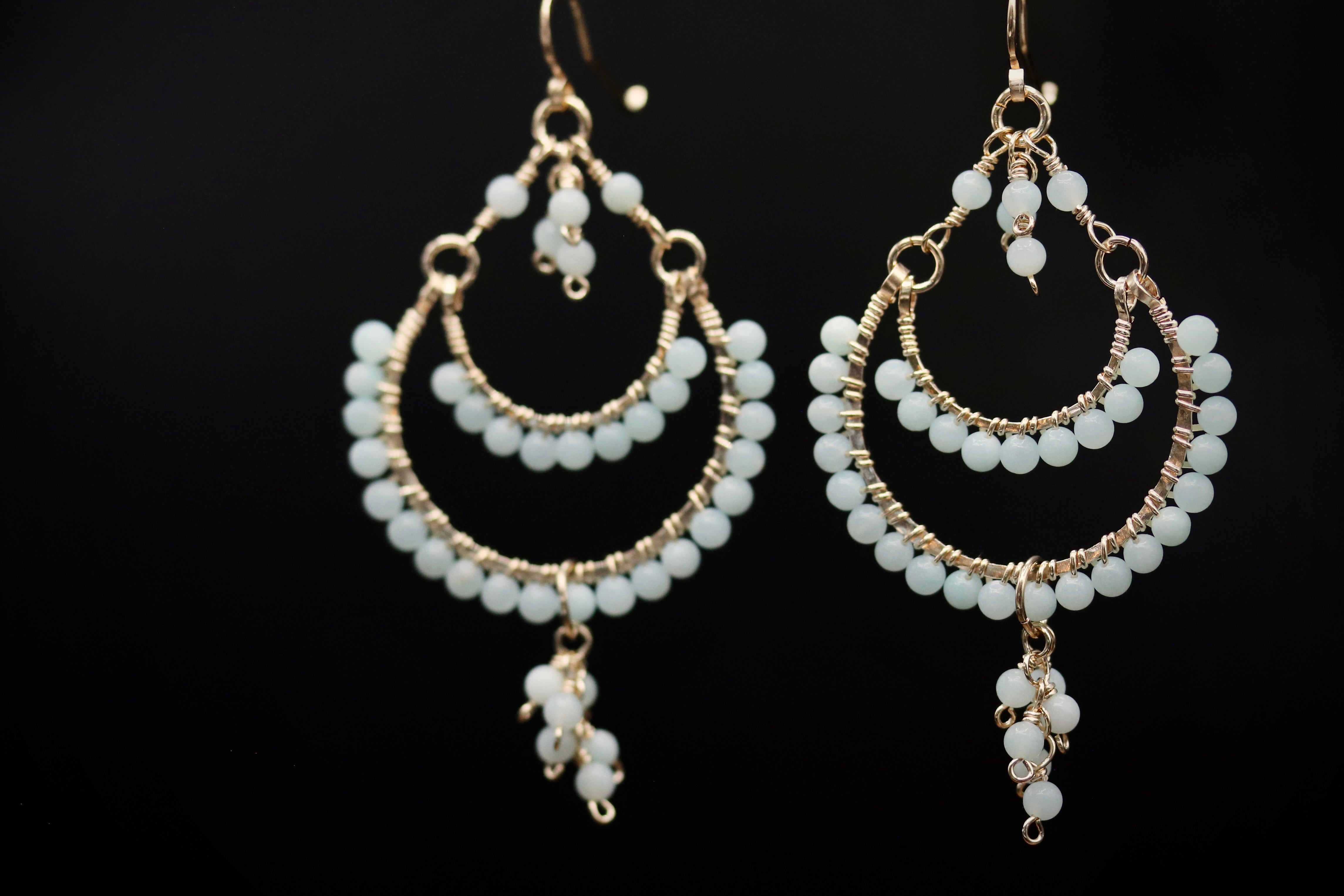 A pair of elegant earrings with white beads and dangling charms against a black background.