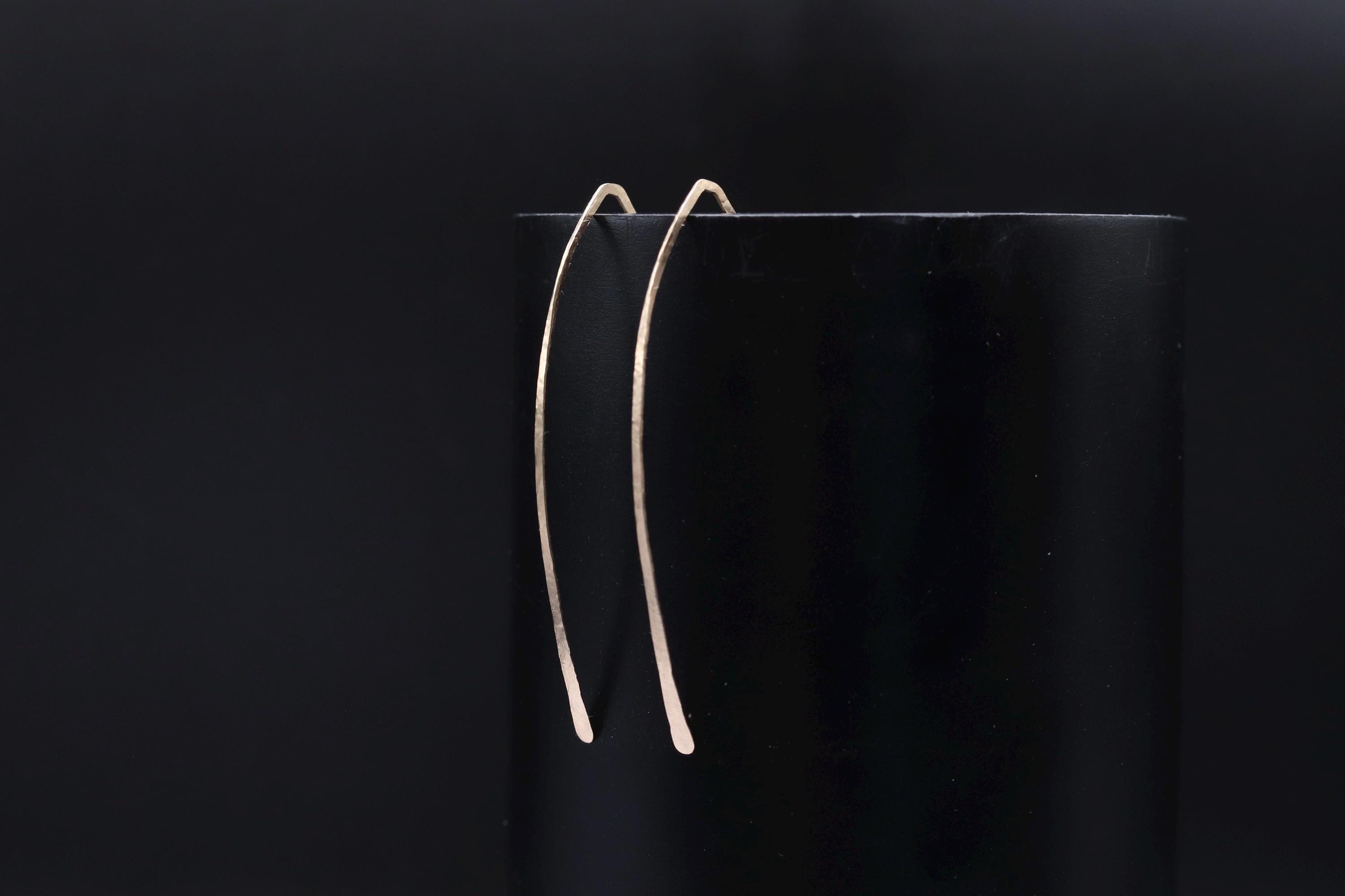 A pair of gold earrings with a curved design, resting on a black surface.