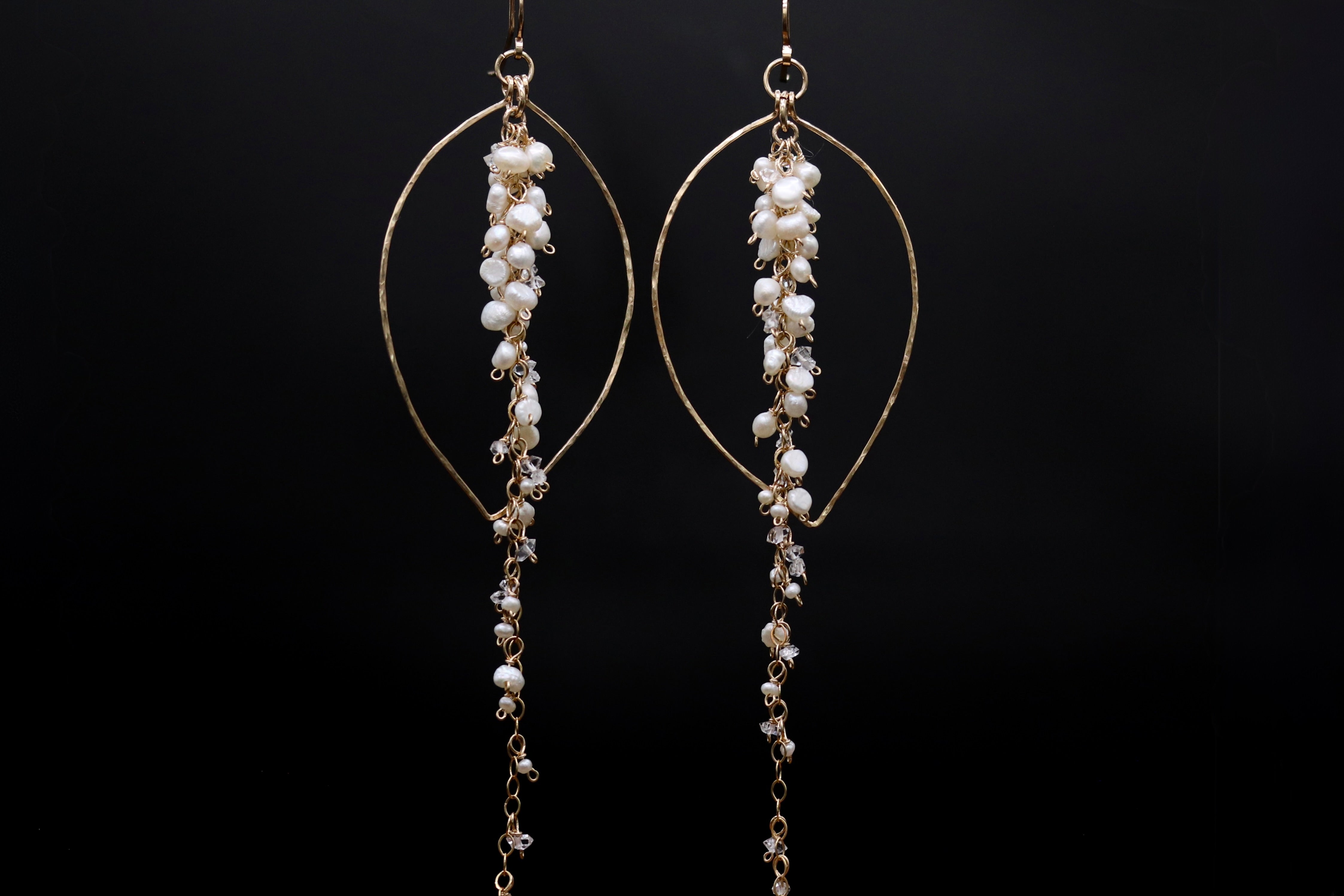 A pair of elegant gold earrings with dangling pearls and crystals against a black background.