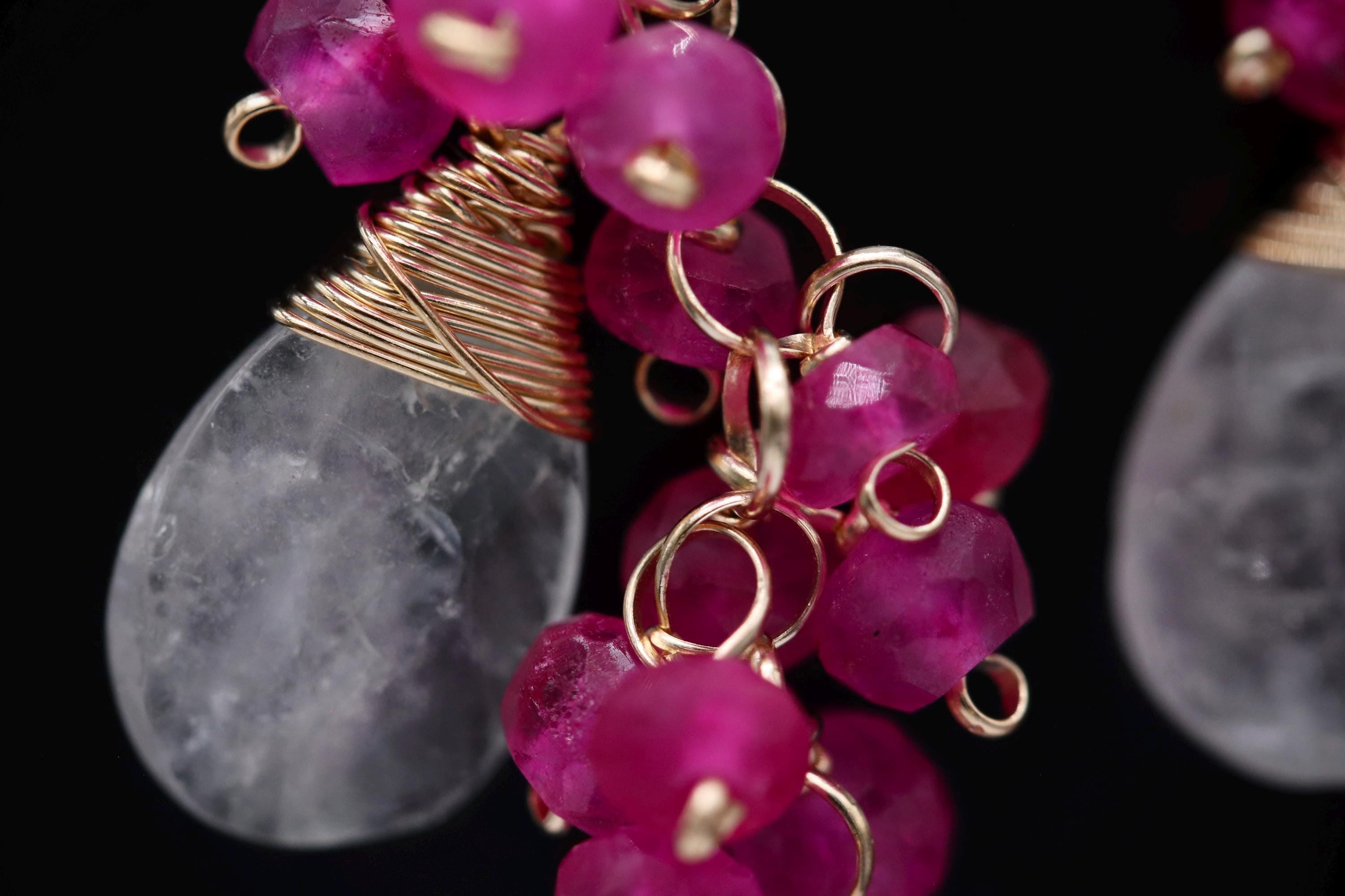 A close-up view of a piece of jewelry, featuring a clear stone pendant with a twisted wire design and a cluster of pink gemstone beads.