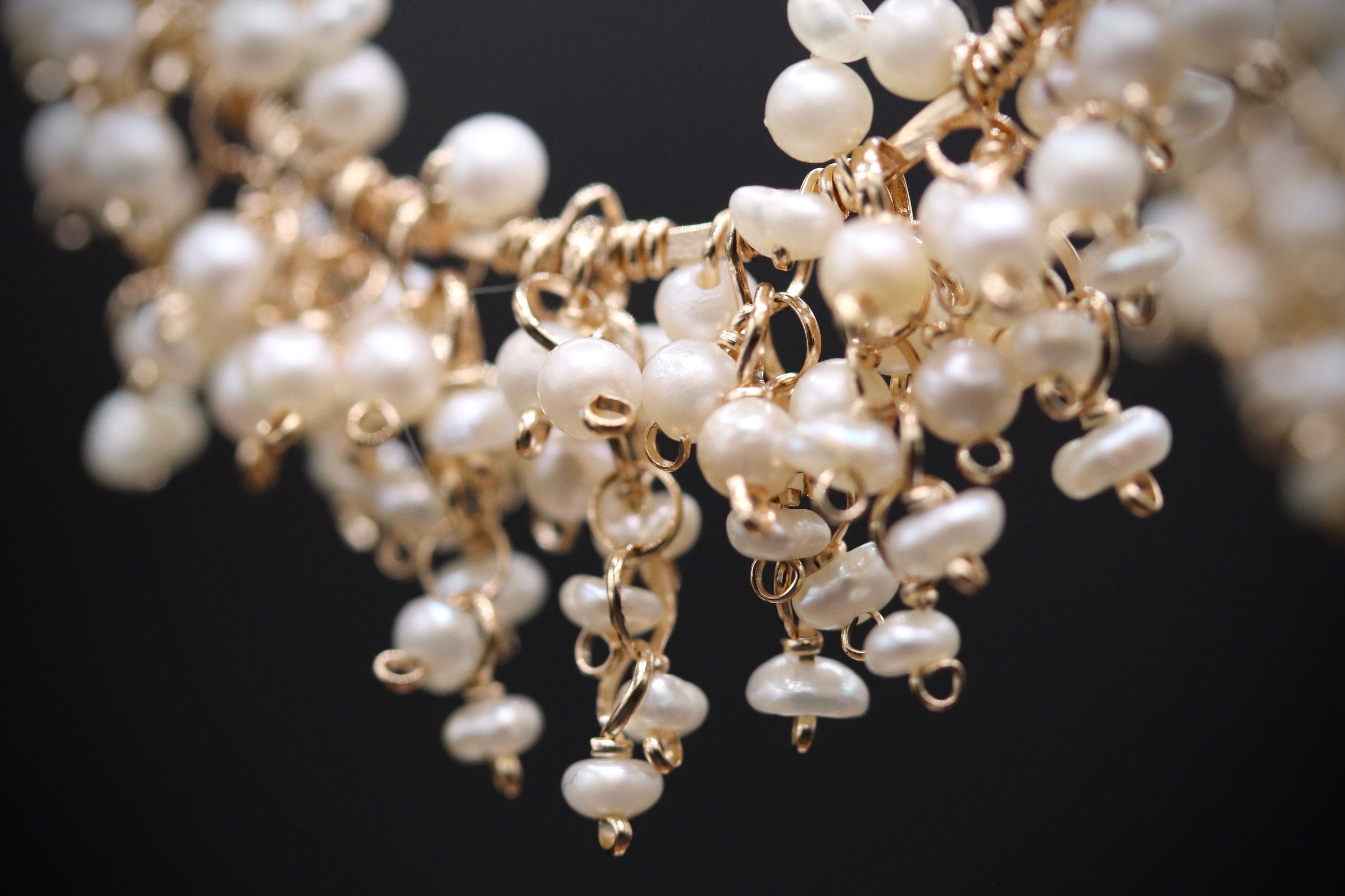 A close-up view of a delicate necklace with numerous small white pearls and gold-colored metal charms hanging from a wire.
