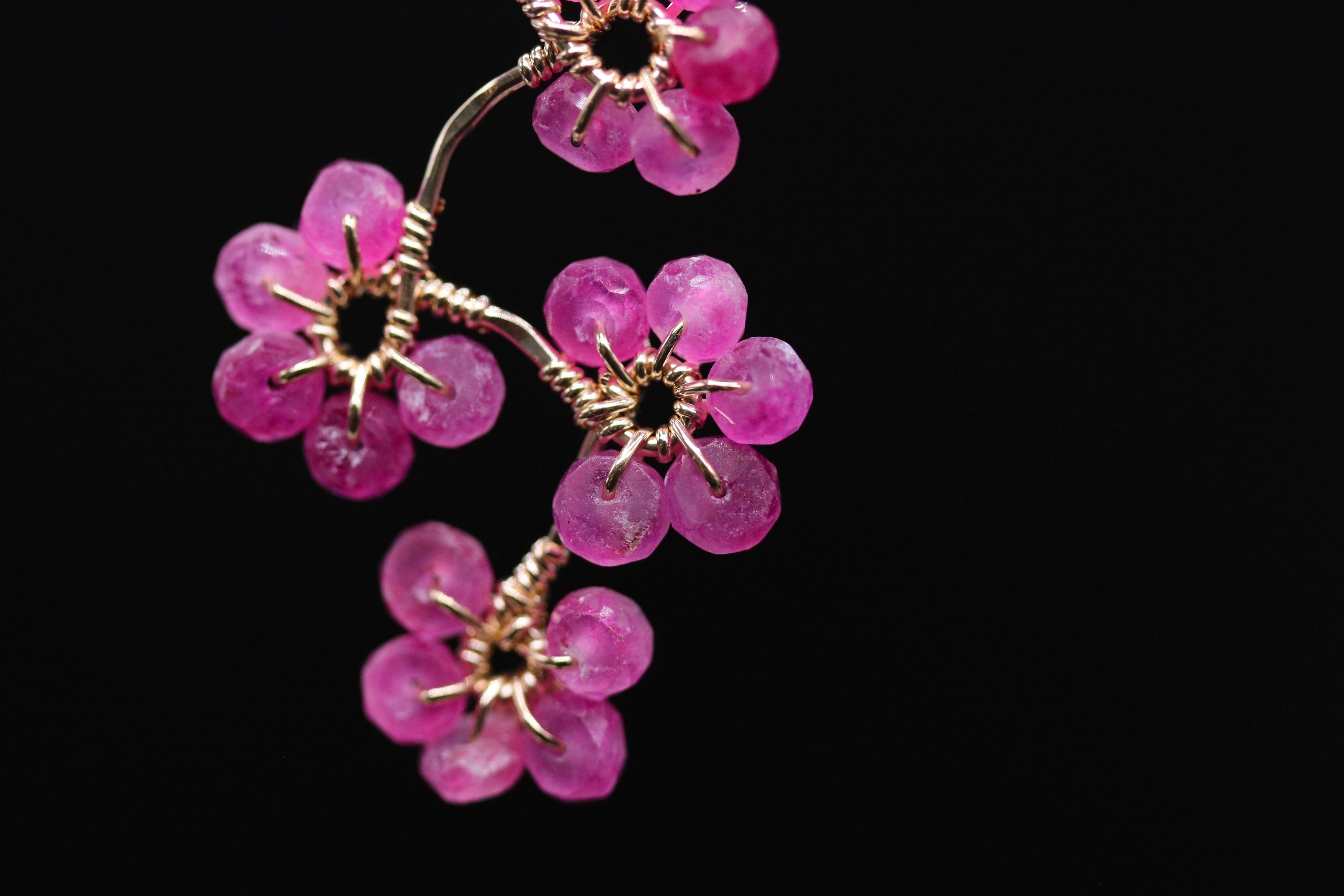 A close-up view of a delicate wire flower-shaped ornament, composed of small, round, pink gemstones or beads, against a dark background.