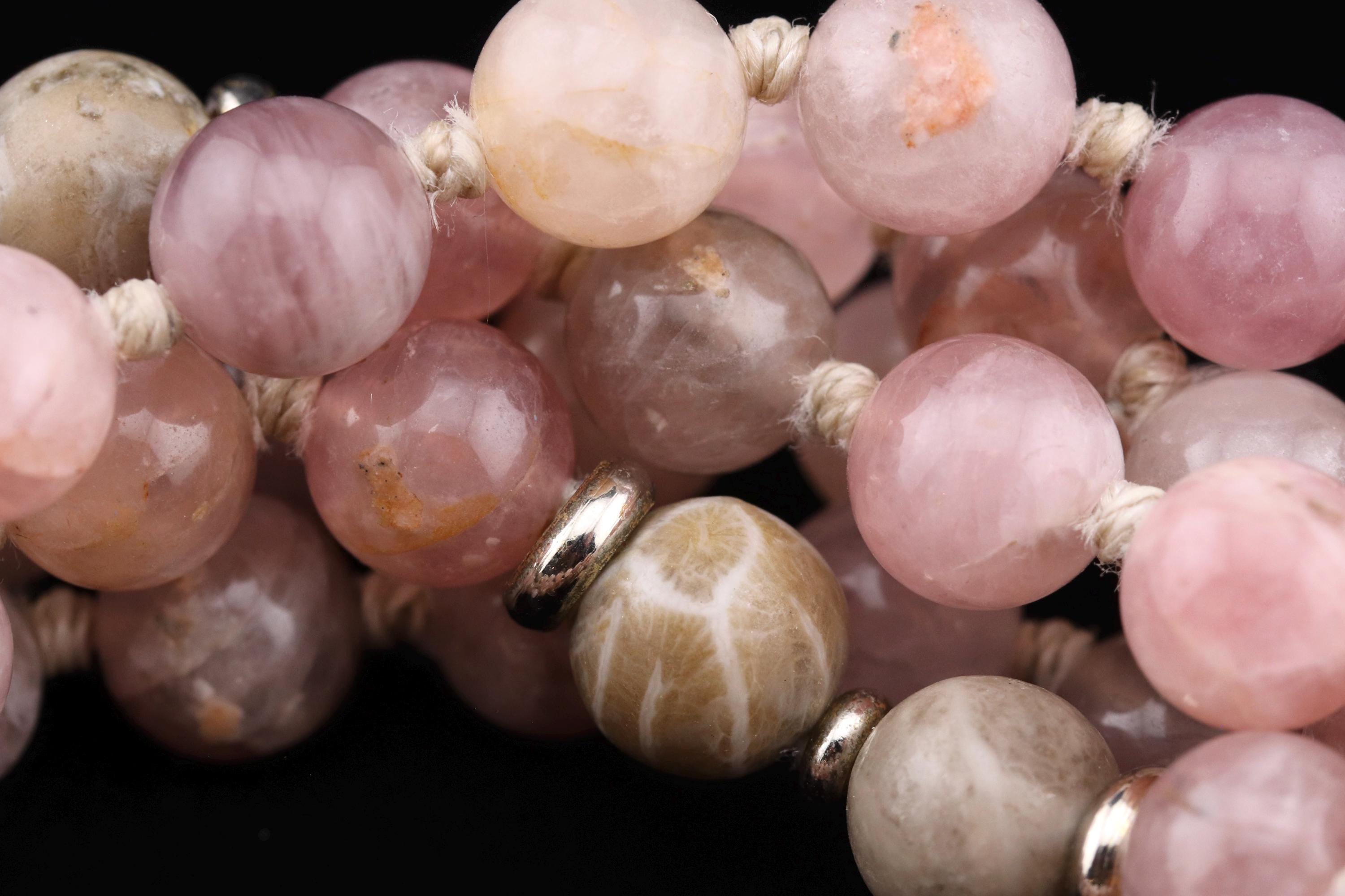 A close-up image of a collection of colorful beads, including pink, white, and beige stones, arranged in a circular pattern.