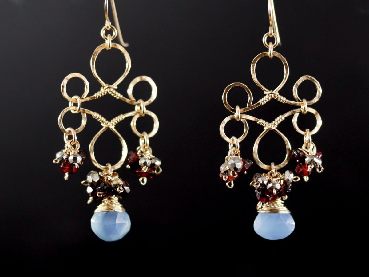 May include: Gold dangle earrings with a delicate, intricate design. The earrings feature a cluster of red and silver beads, and a light blue gemstone.