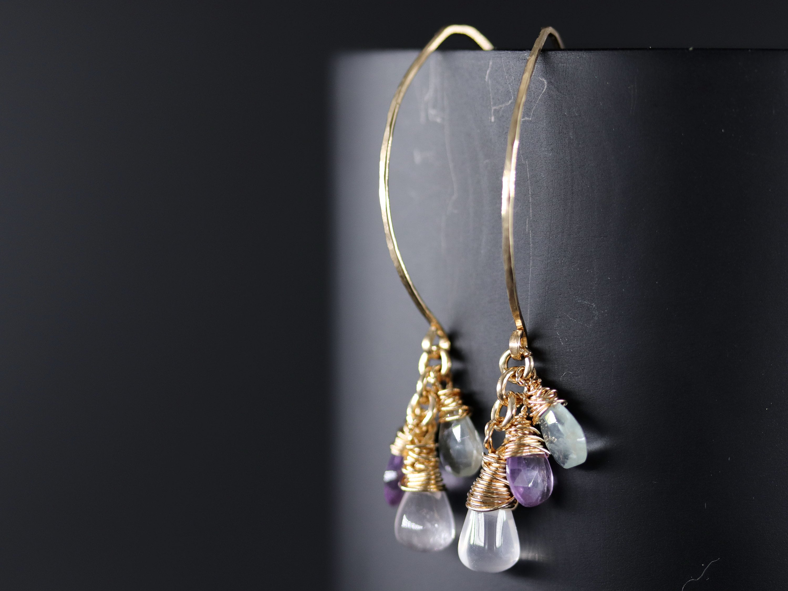 May include: Gold hoop earrings with a cluster of amethyst, aquamarine, and clear quartz stones dangling from the bottom.