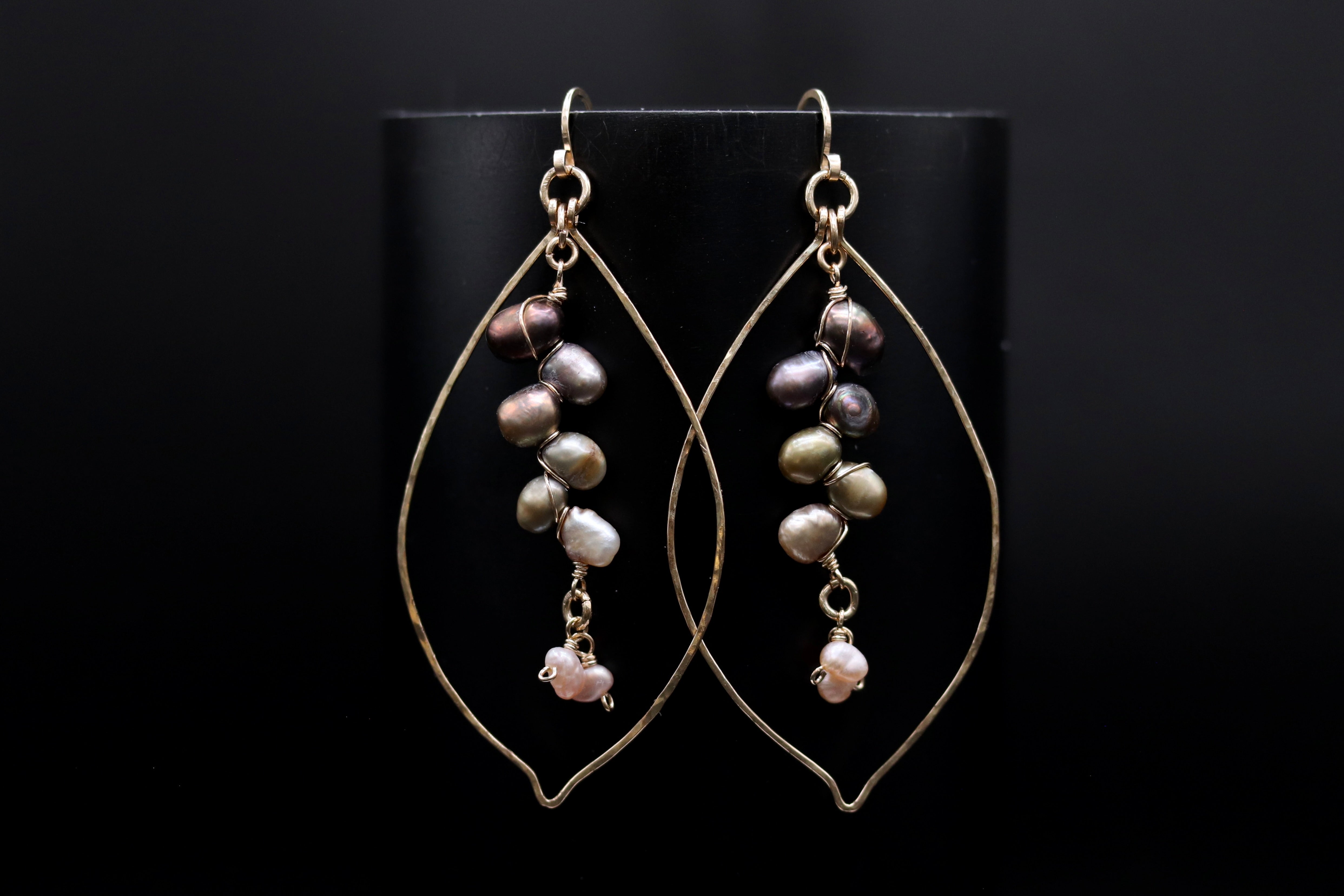 A pair of gold earrings with pearls hanging from the ends, displayed against a black background.