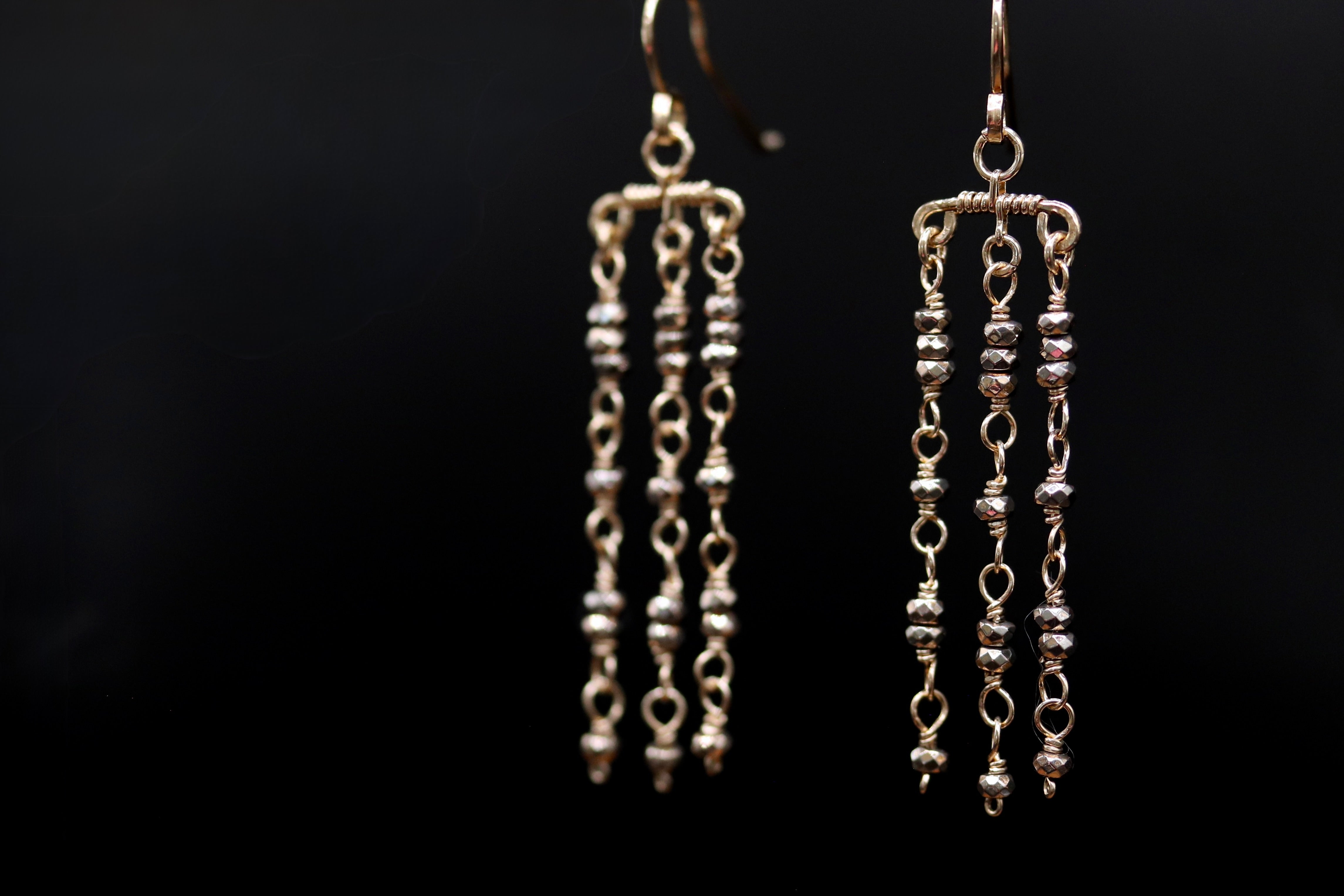 A pair of silver earrings with multiple tiers of small beads hanging from them against a black background.