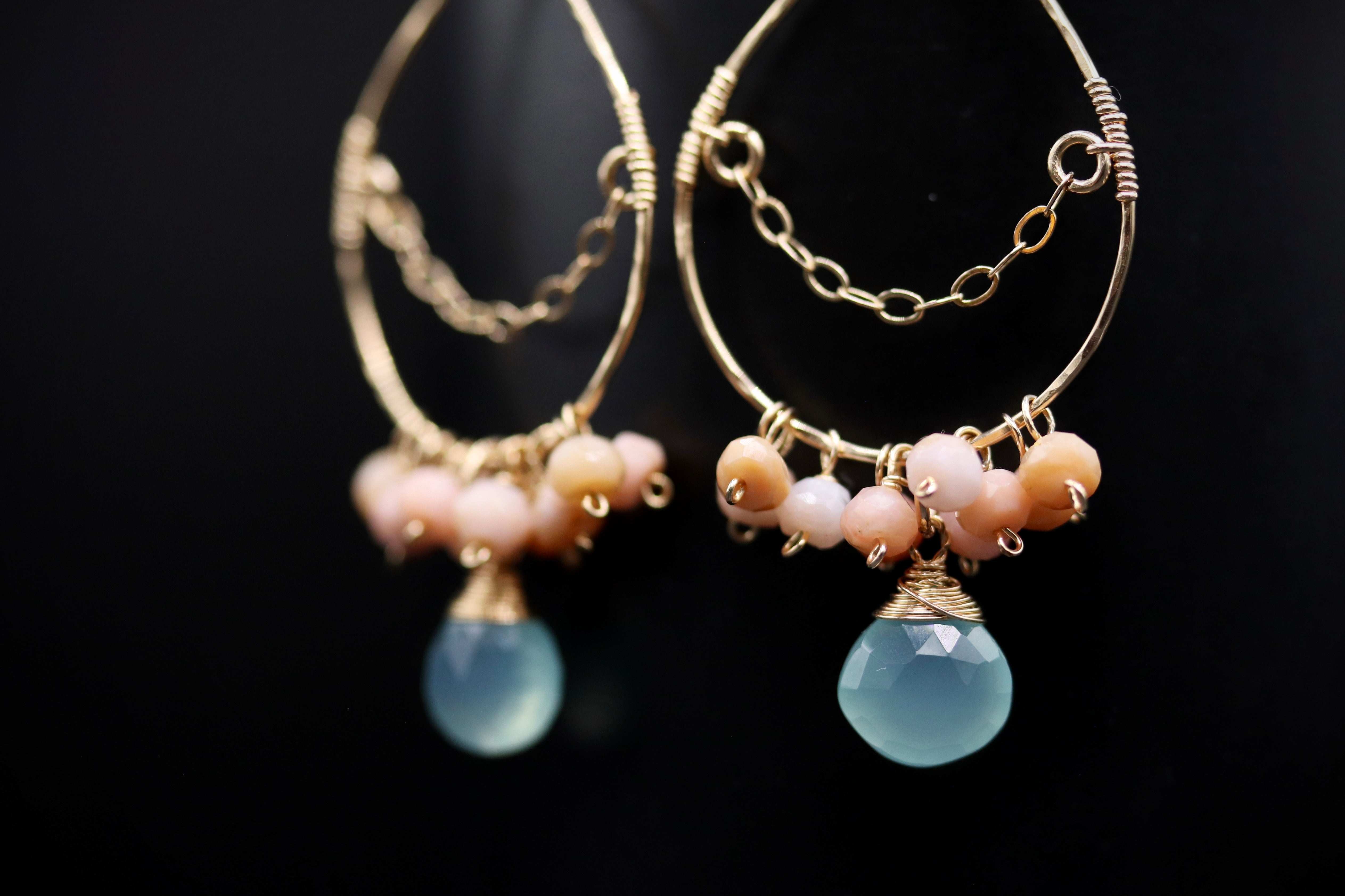 A pair of gold hoop earrings with blue and pink gemstone beads hanging from them.