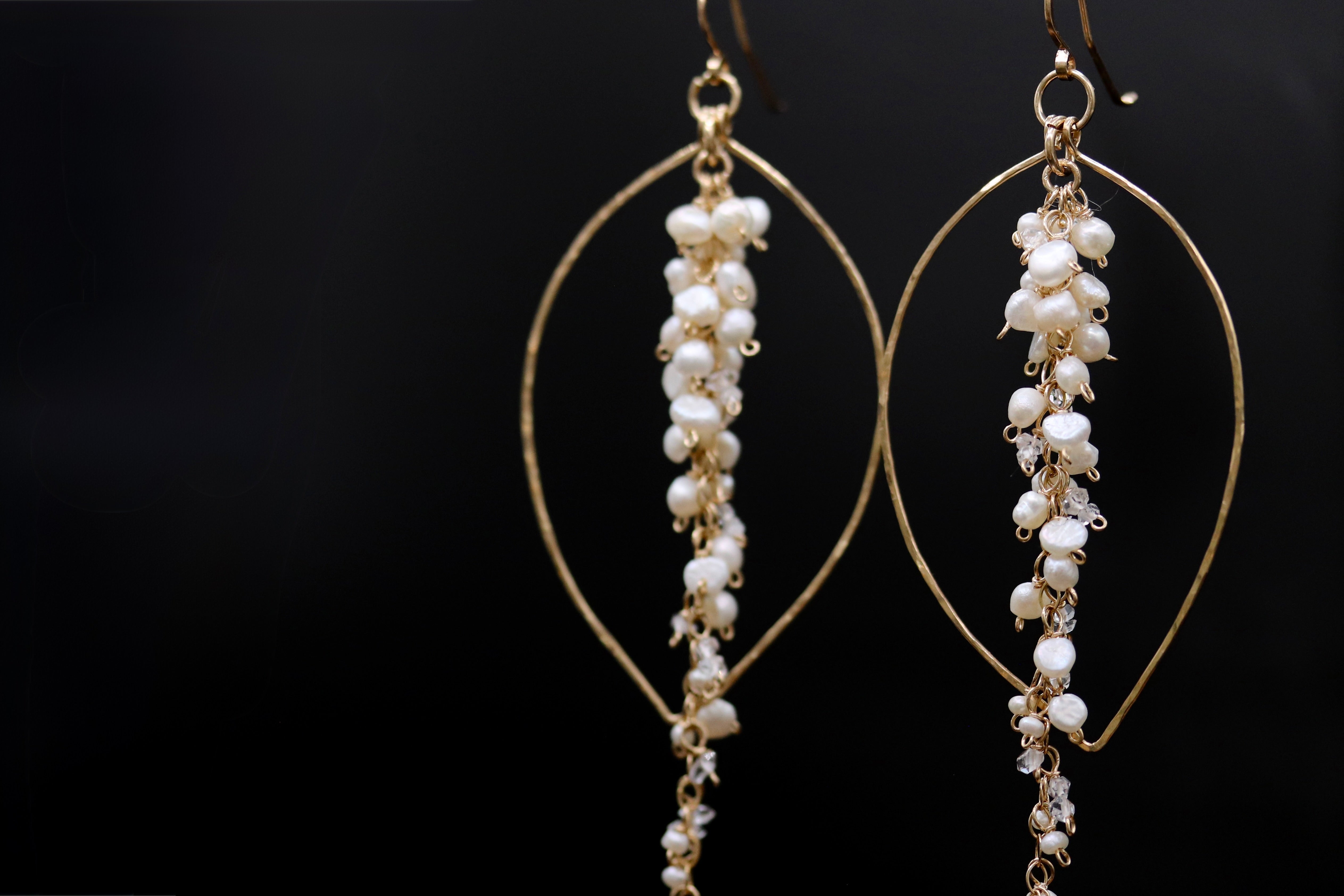 A pair of elegant gold earrings with white pearls hanging from the ends, set against a dark background.