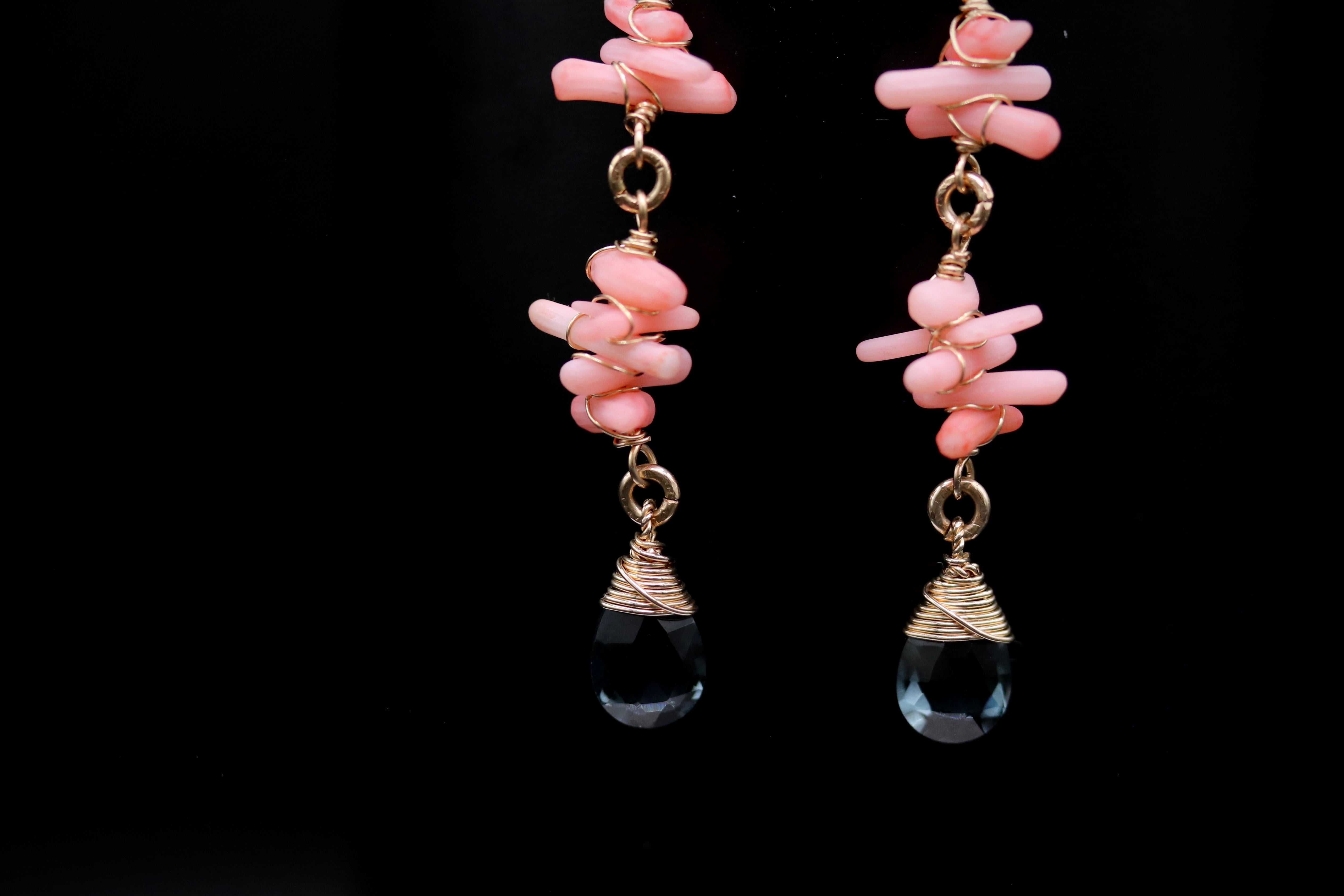 A pair of earrings with pink and clear gemstone-like elements, suspended from gold chains against a black background.
