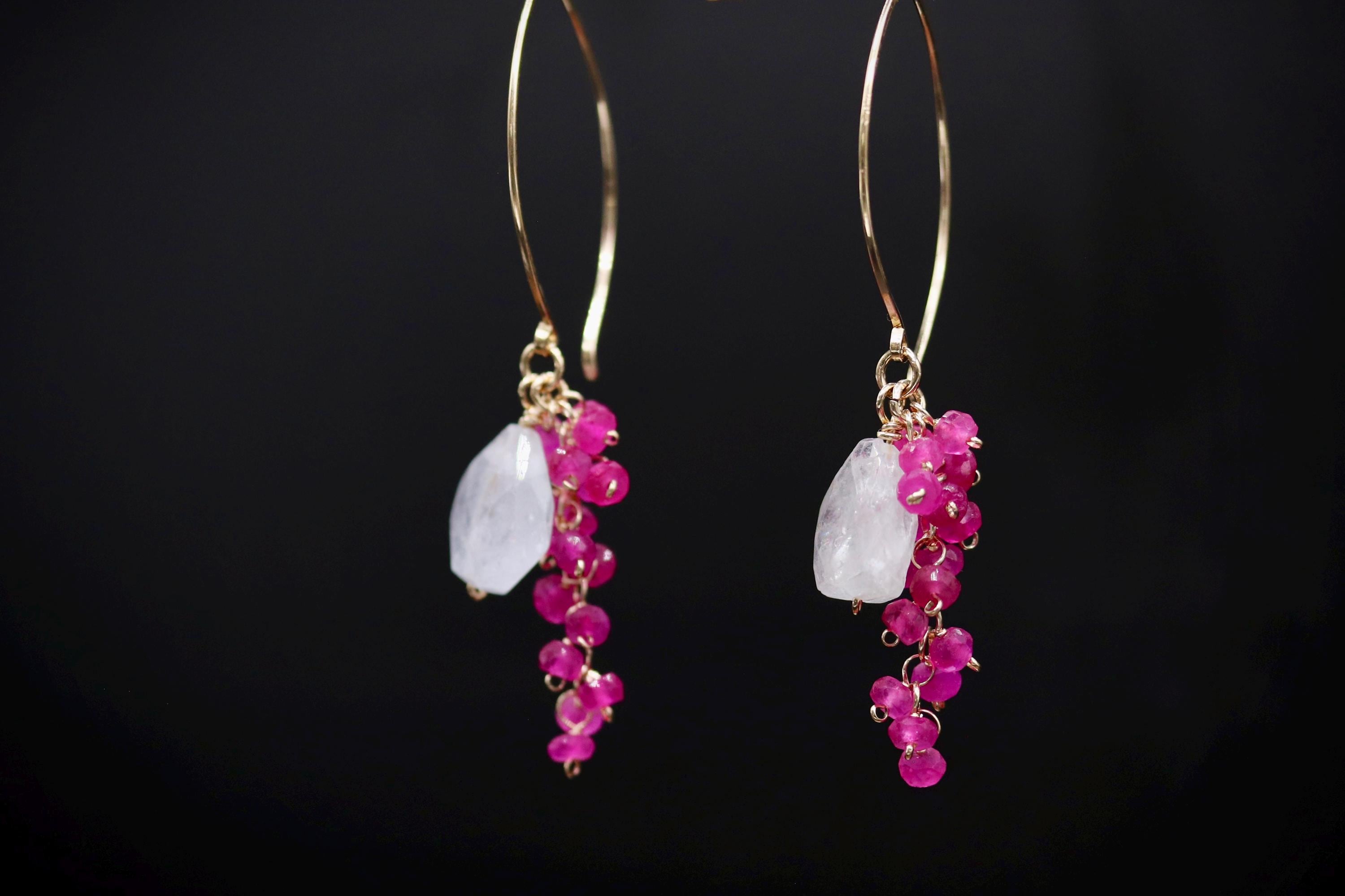 A pair of gold hoop earrings with pink gemstones hanging from them against a black background.
