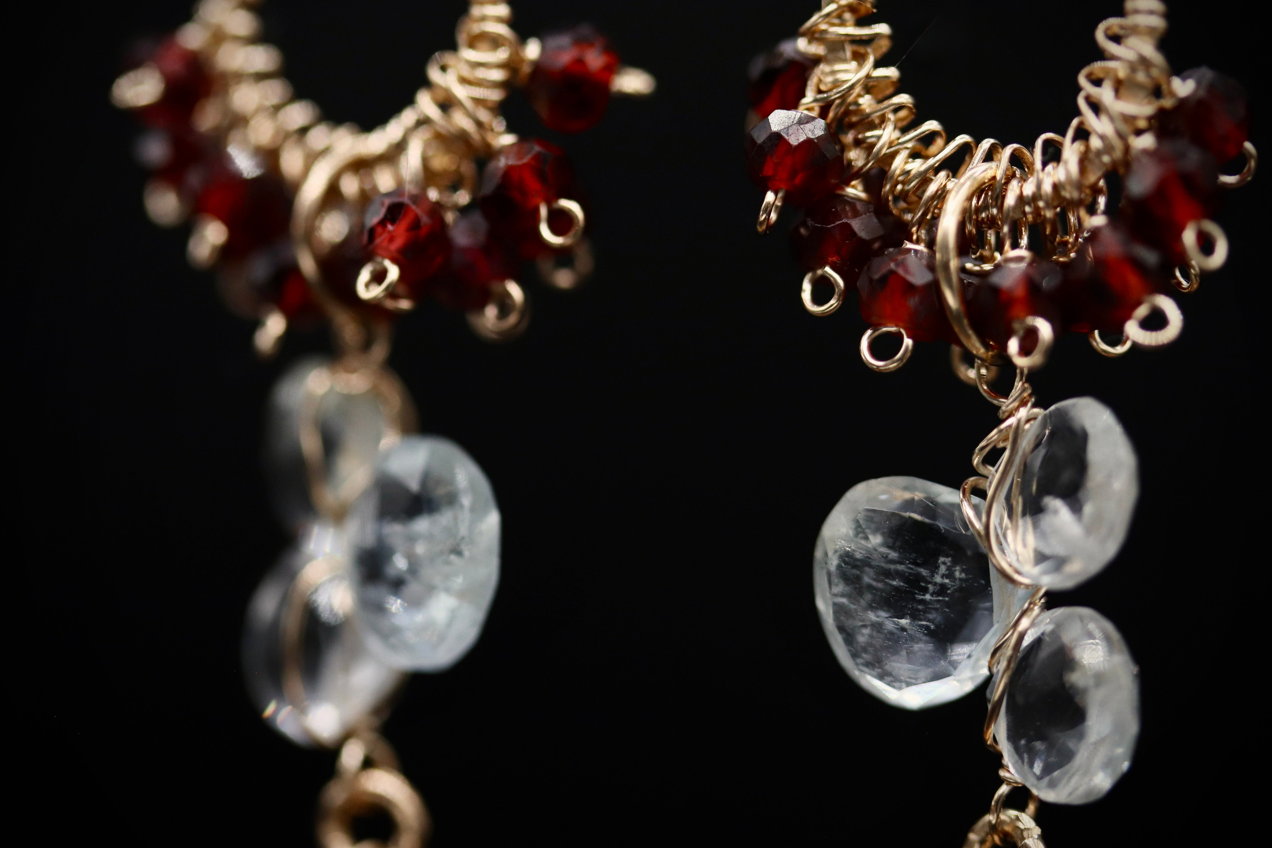 a close-up view of two ornate earrings with a combination of clear and red gemstones, as well as gold-colored metal elements.