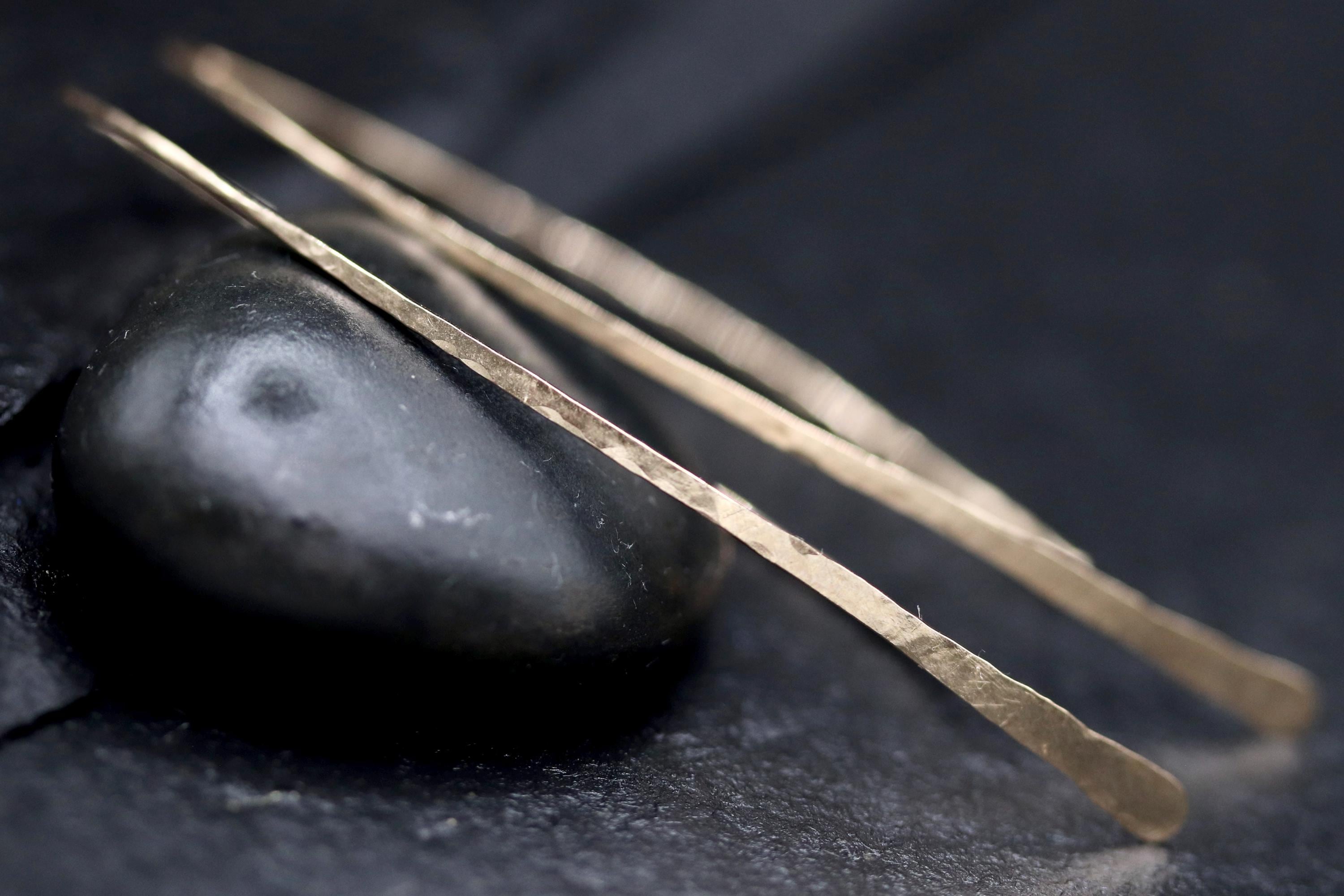 a close-up view of a pair of gold earrings resting on a black surface, with a dark background.