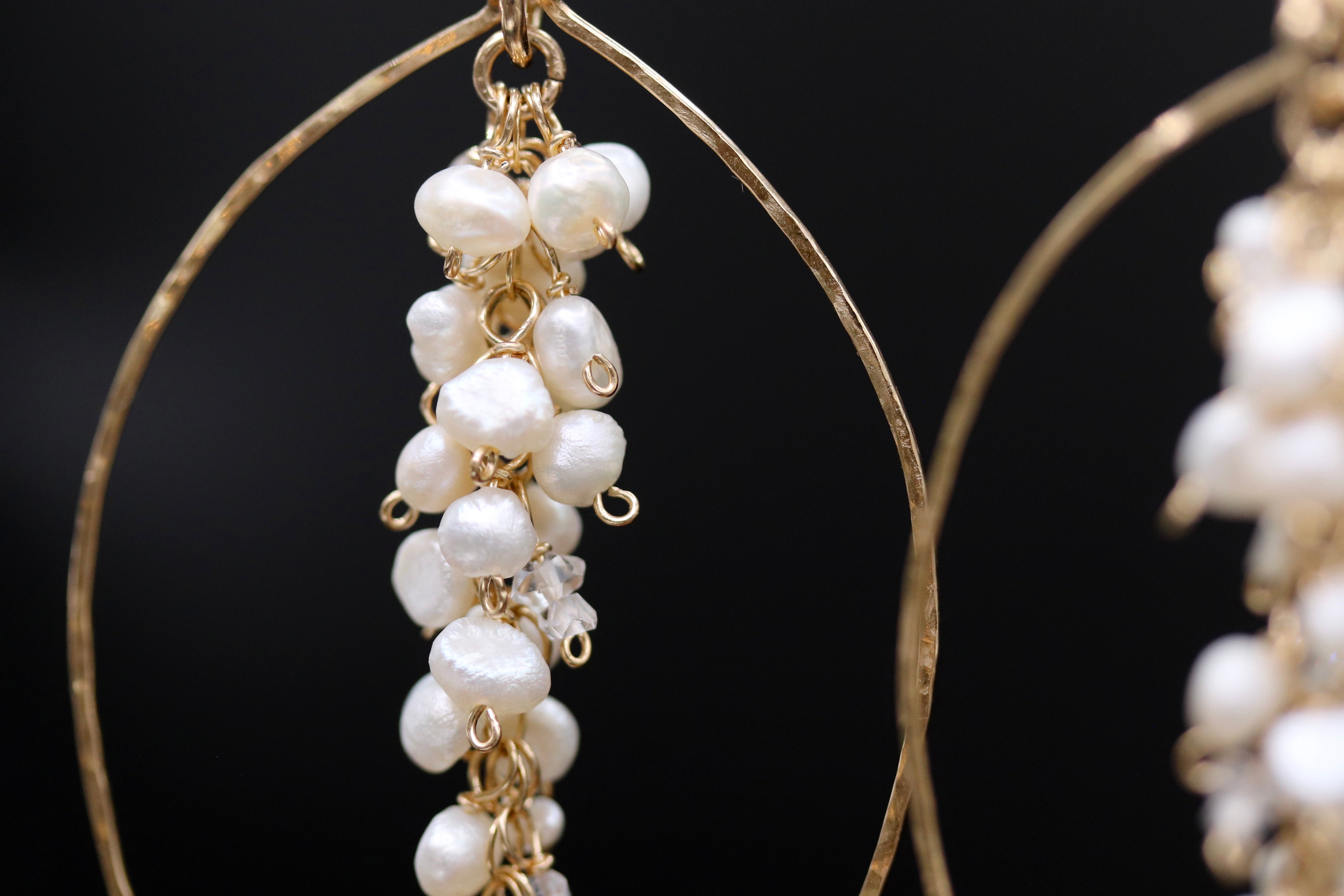 A close-up view of a pair of gold hoop earrings with white pearls hanging from them.