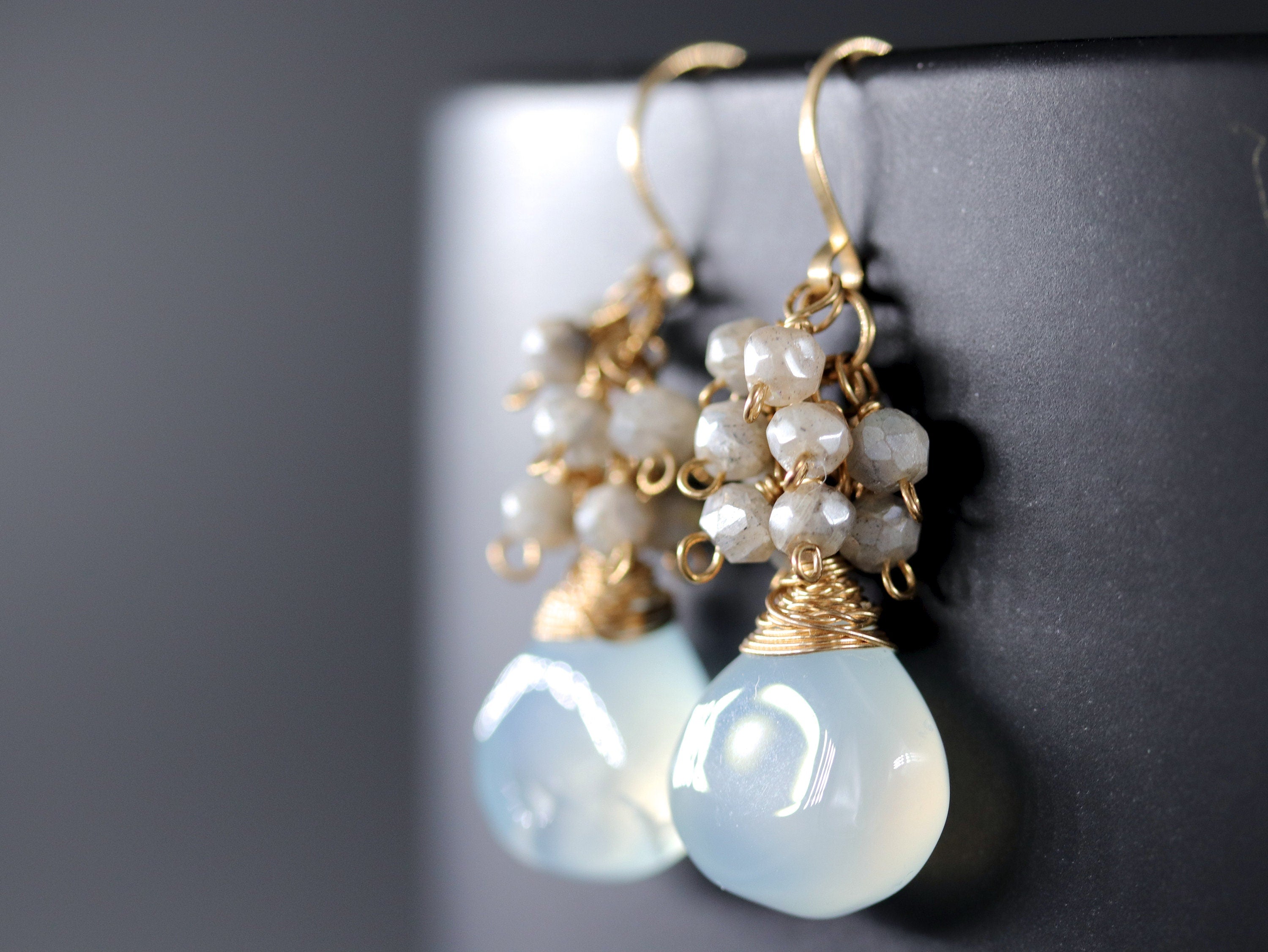 May include: Gold earrings with a light blue teardrop-shaped gemstone and a cluster of small white beads.
