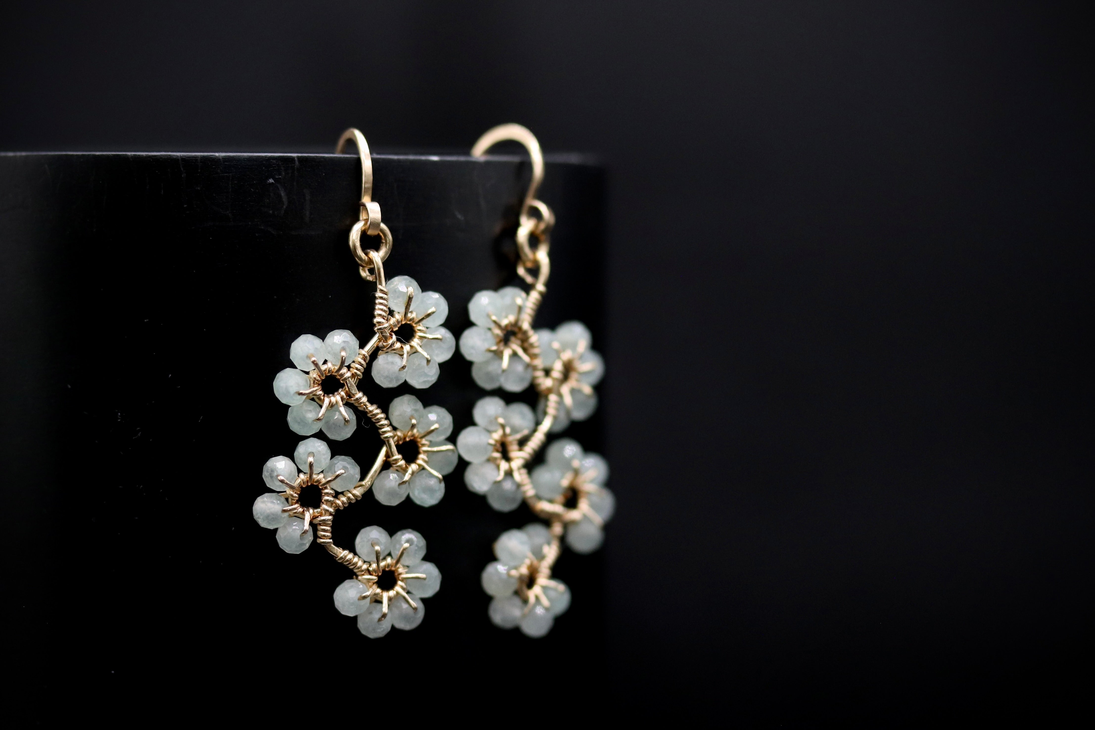 A pair of delicate earrings with small white flower-shaped charms hanging from a black background.