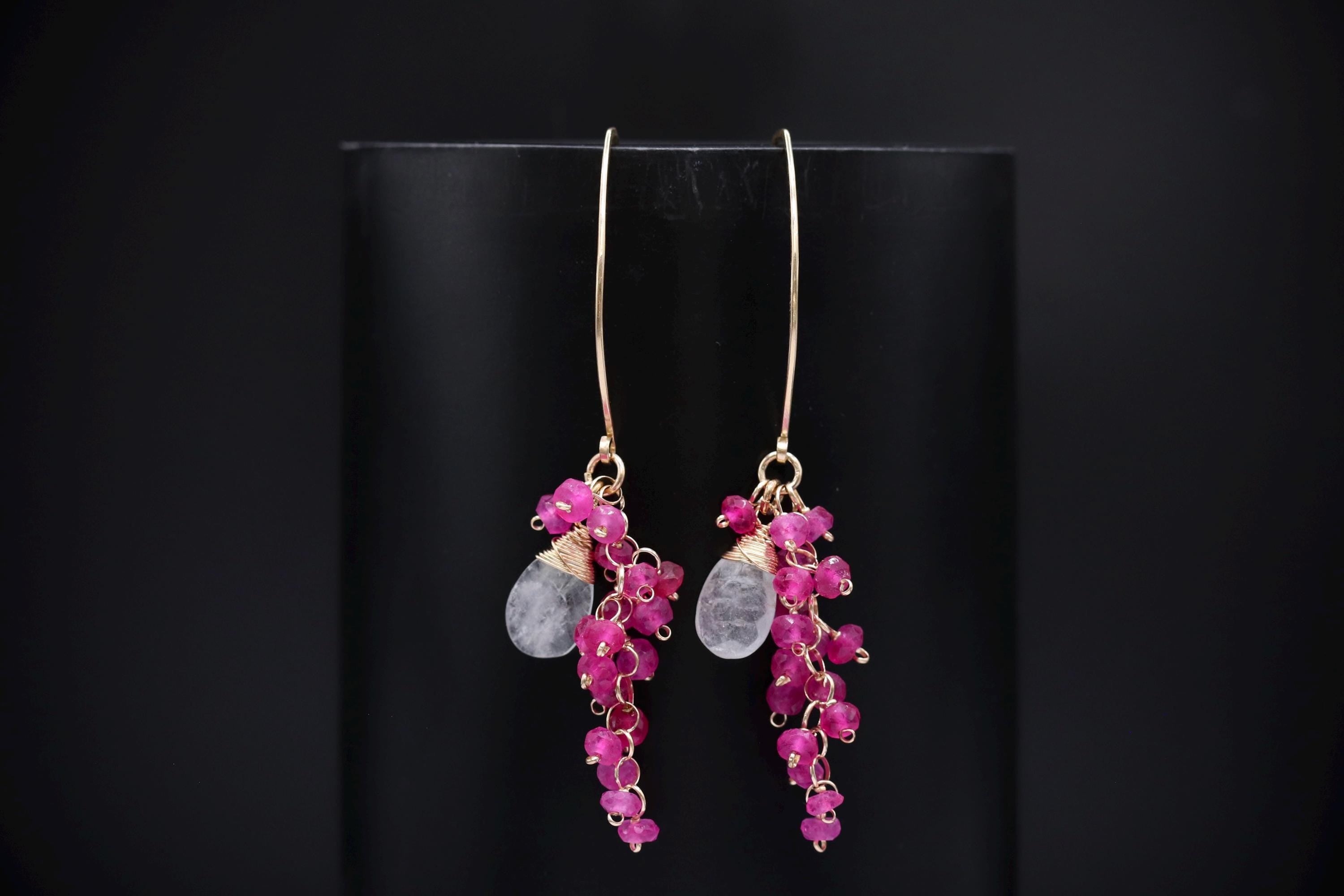 A pair of elegant earrings with a combination of pink gemstones and metallic beads, displayed against a black background.