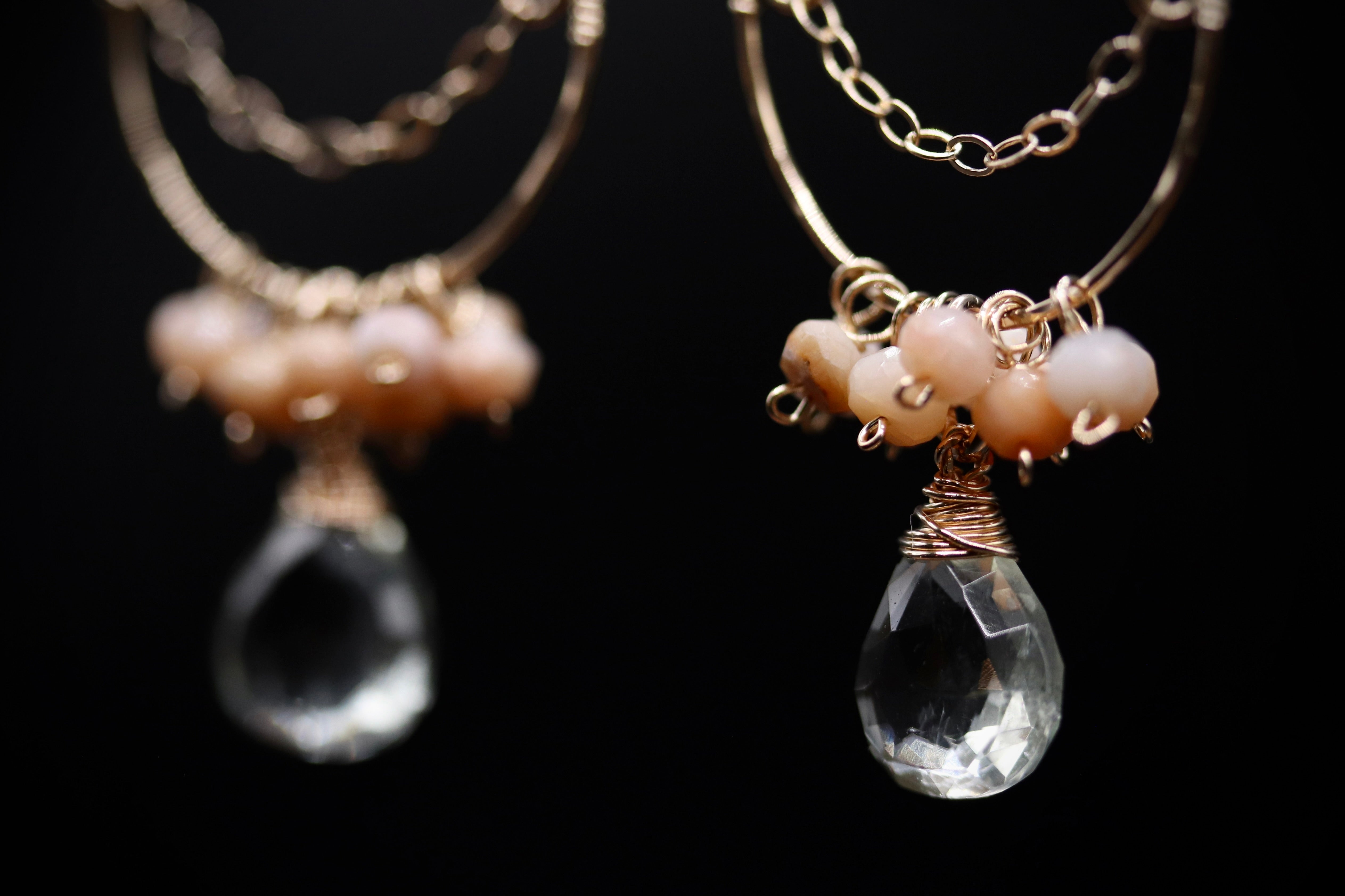 A pair of elegant earrings with clear crystal droplets and beaded accents, set against a dark background.