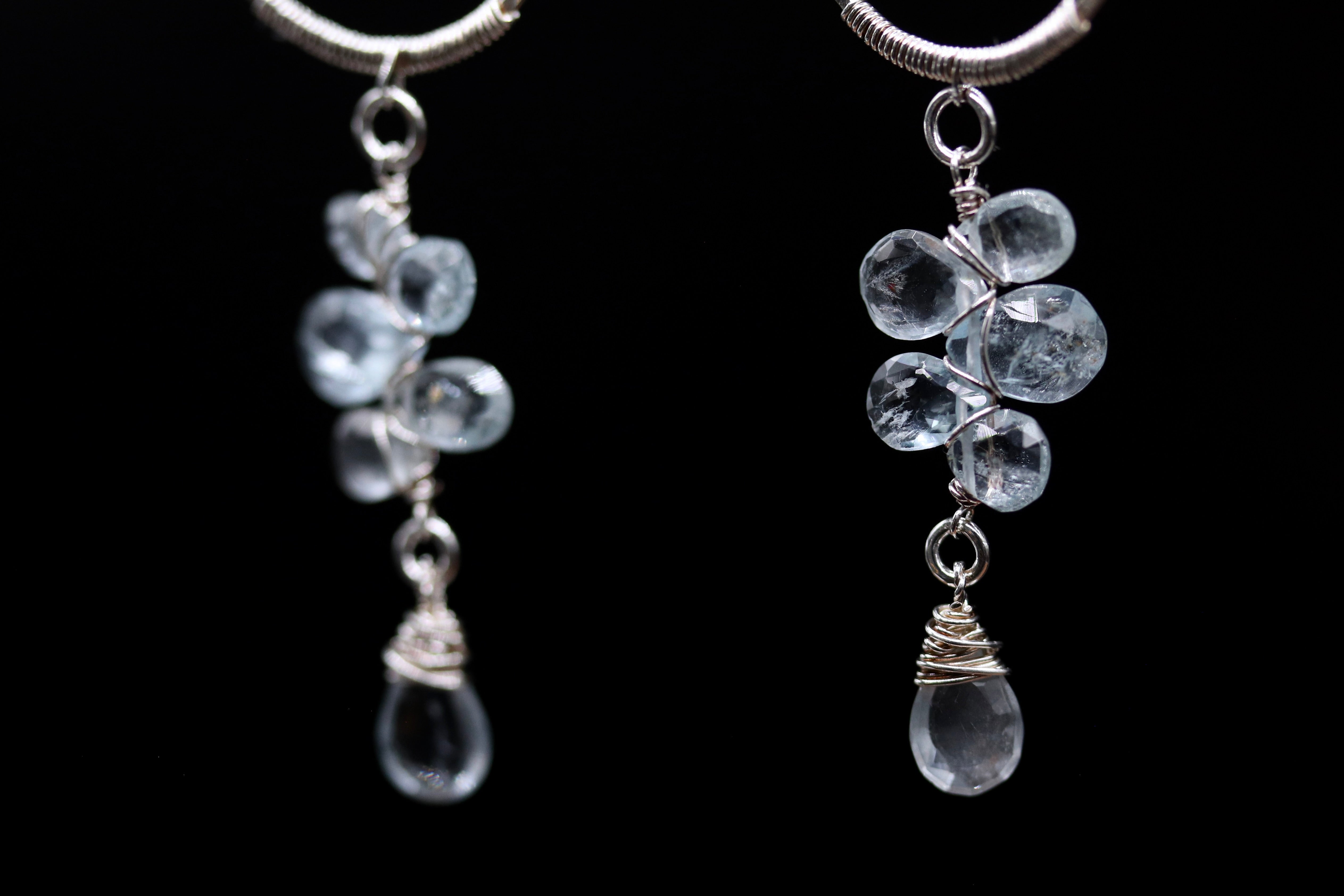 A pair of elegant earrings with clear crystal stones and silver wire accents, hanging against a black background.