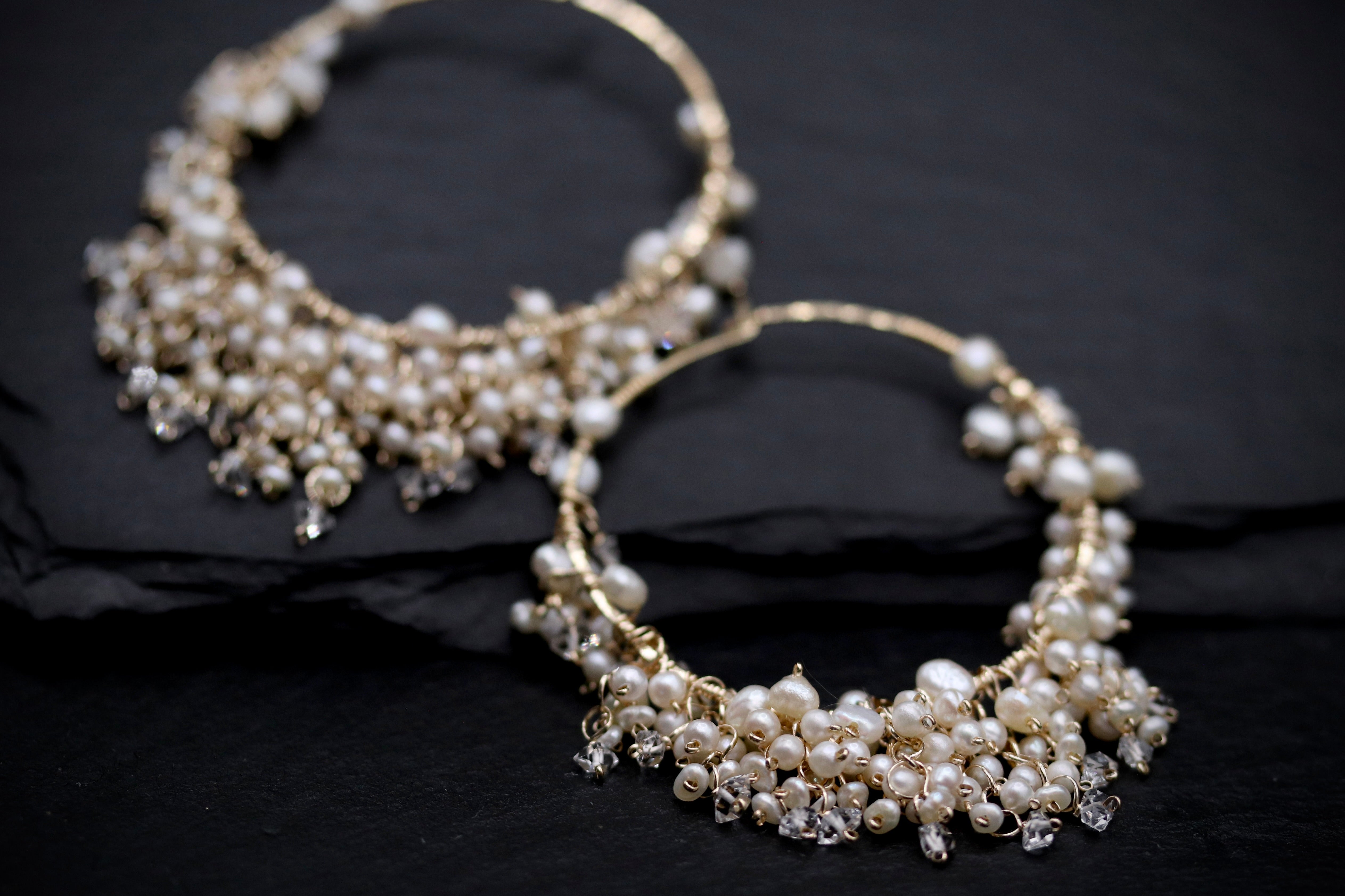 two ornate earrings with a combination of pearls and crystals, set against a dark background.