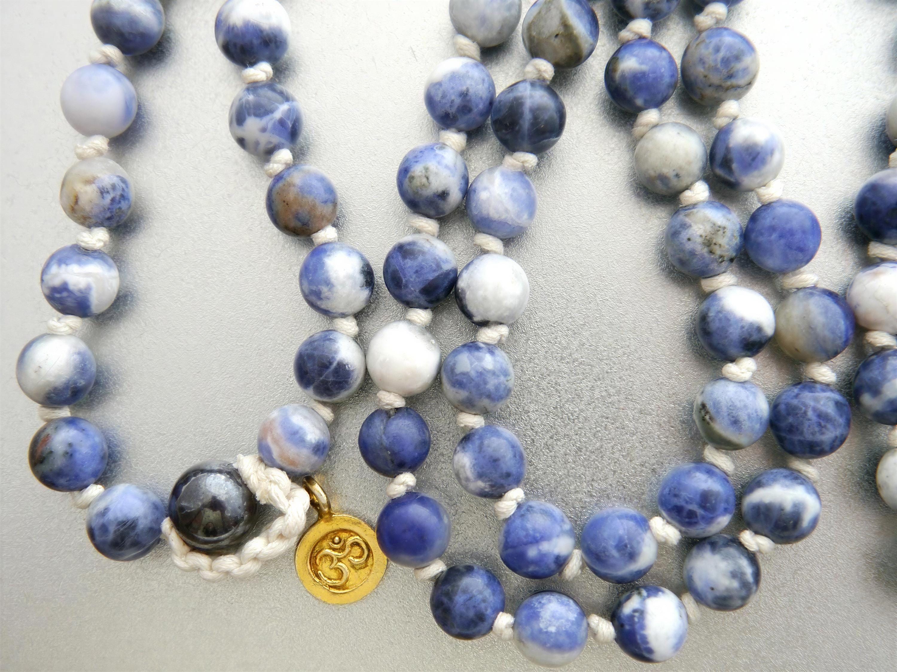 A close-up image of a beaded necklace with blue and white stones, featuring a gold pendant.