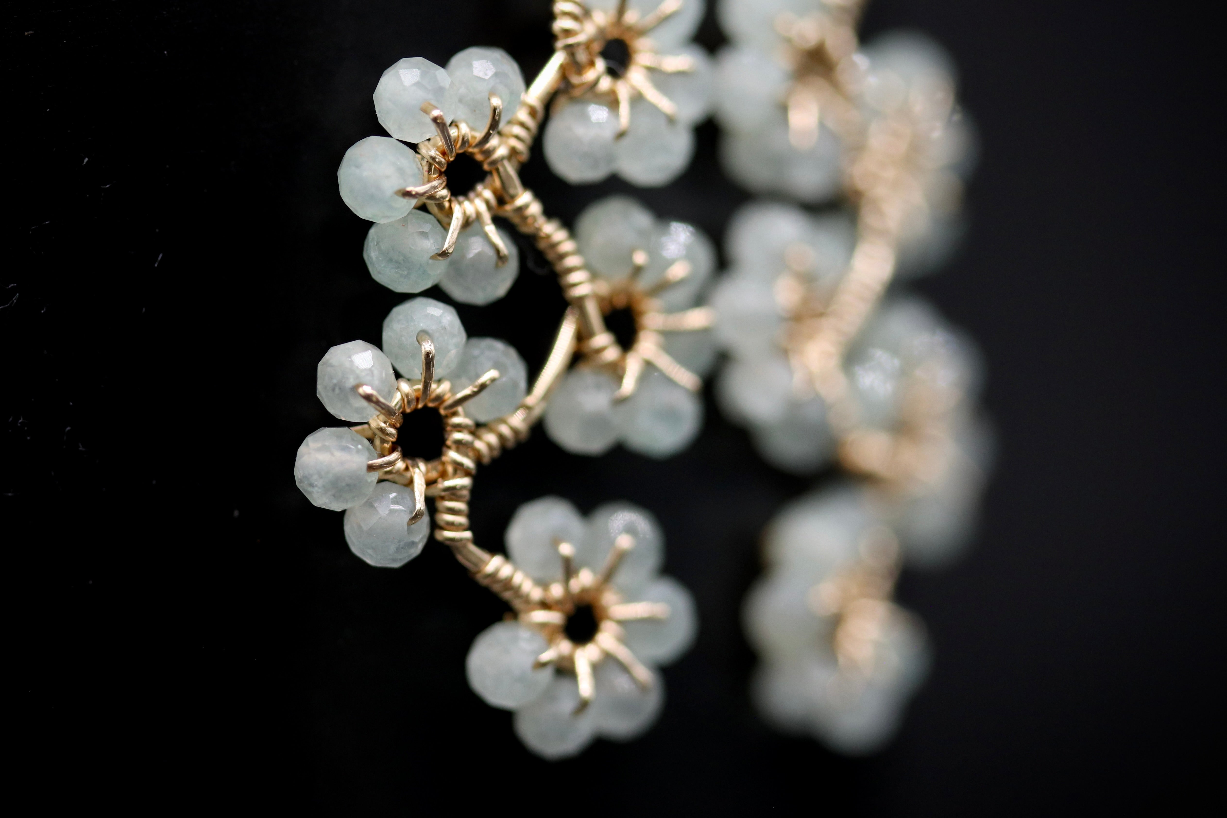 A close-up view of a delicate, intricate piece of jewelry featuring a cluster of small, white, gemstone-like flowers or buds, with a metallic, twisted design.