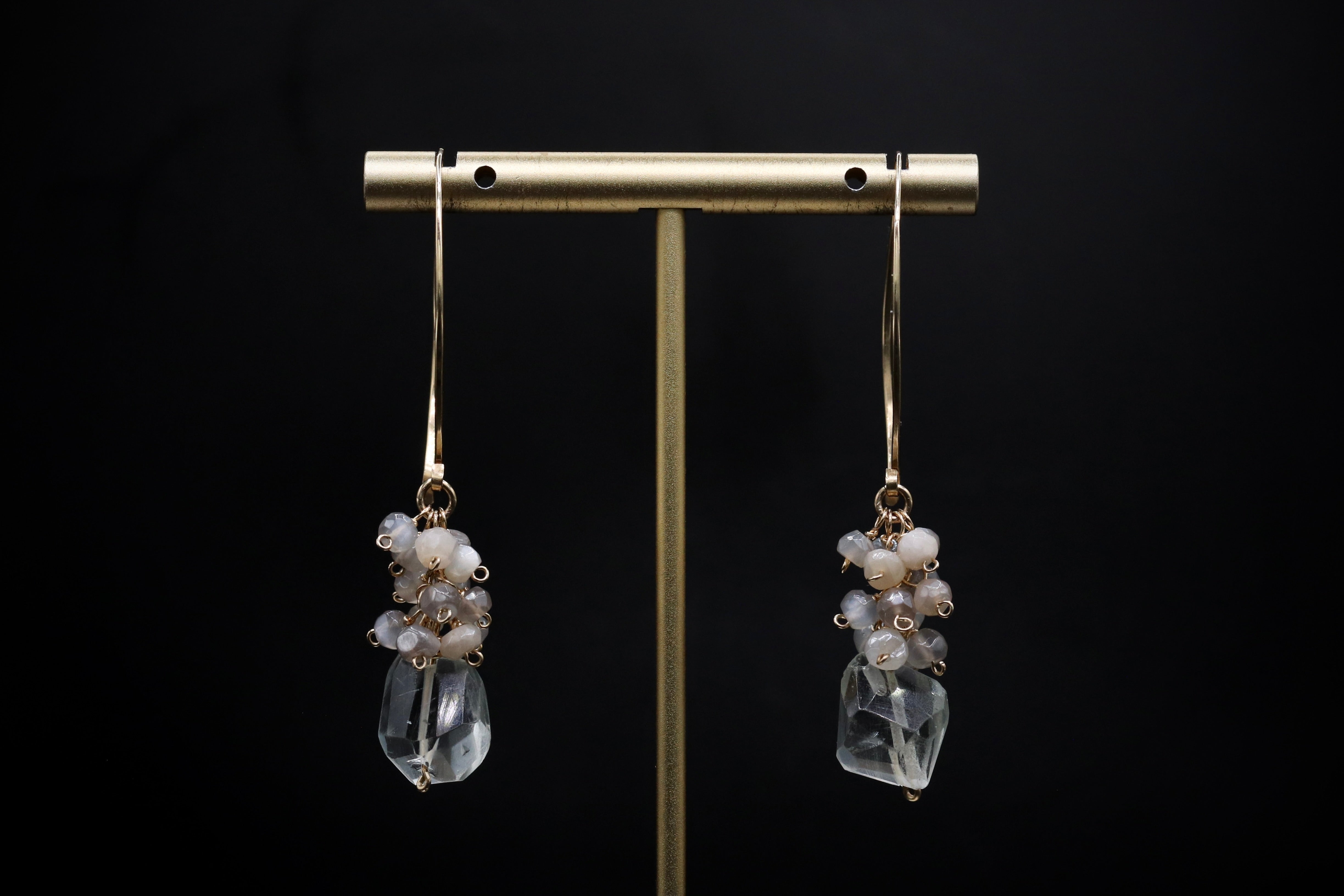 A pair of elegant earrings with clear gemstone accents hanging from a gold metal stand against a black background.