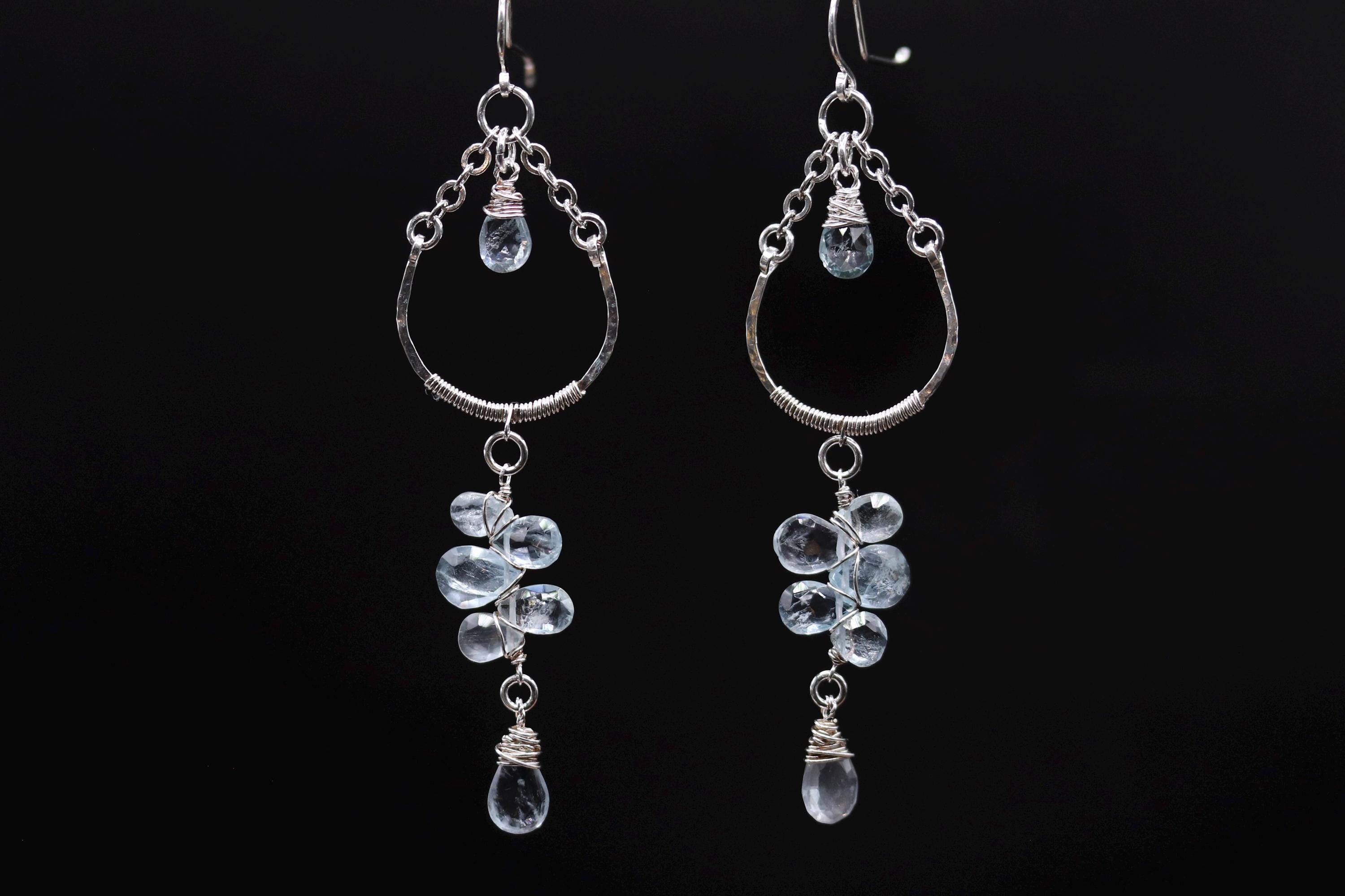 A pair of elegant earrings with clear gemstone accents hanging from the bottom of the earrings against a black background.