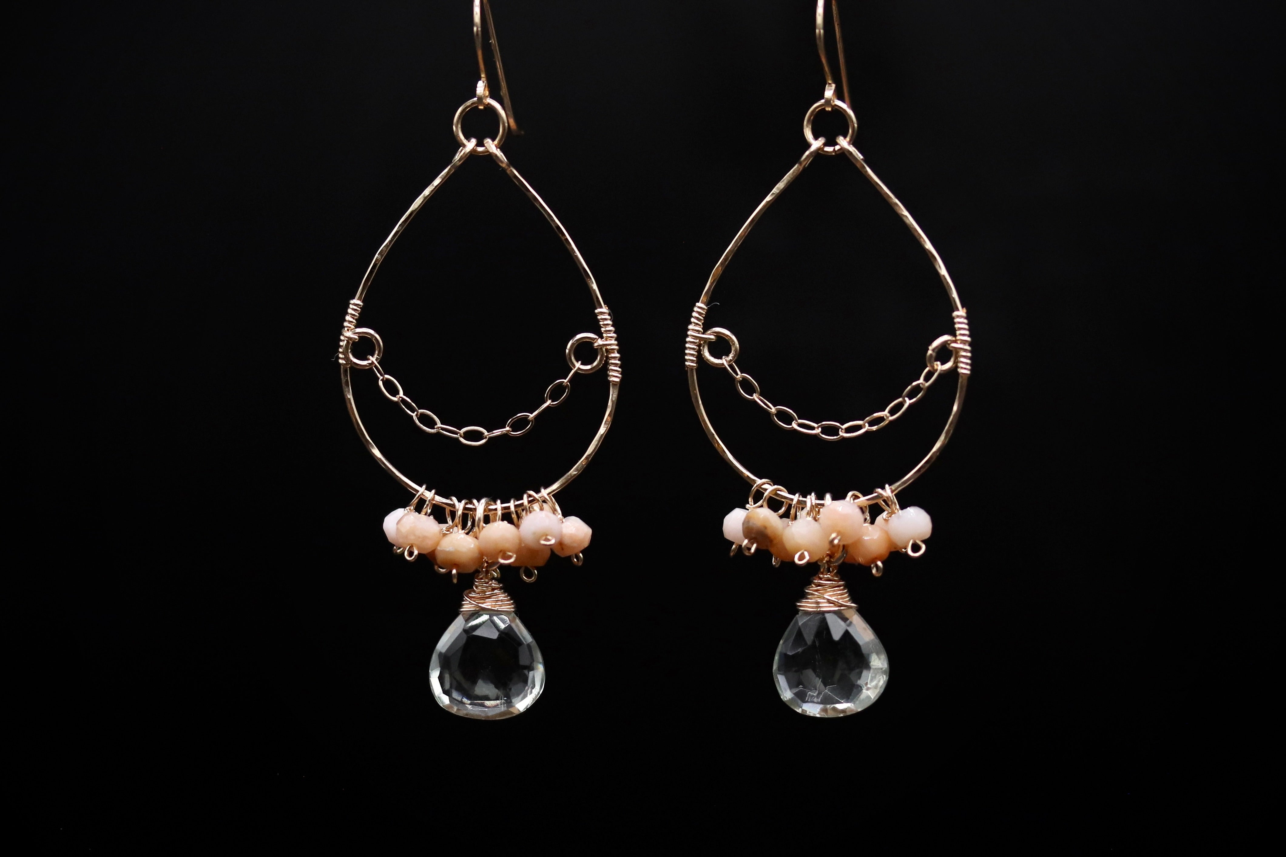 A pair of elegant earrings with a clear crystal pendant and beaded accents, set against a black background.