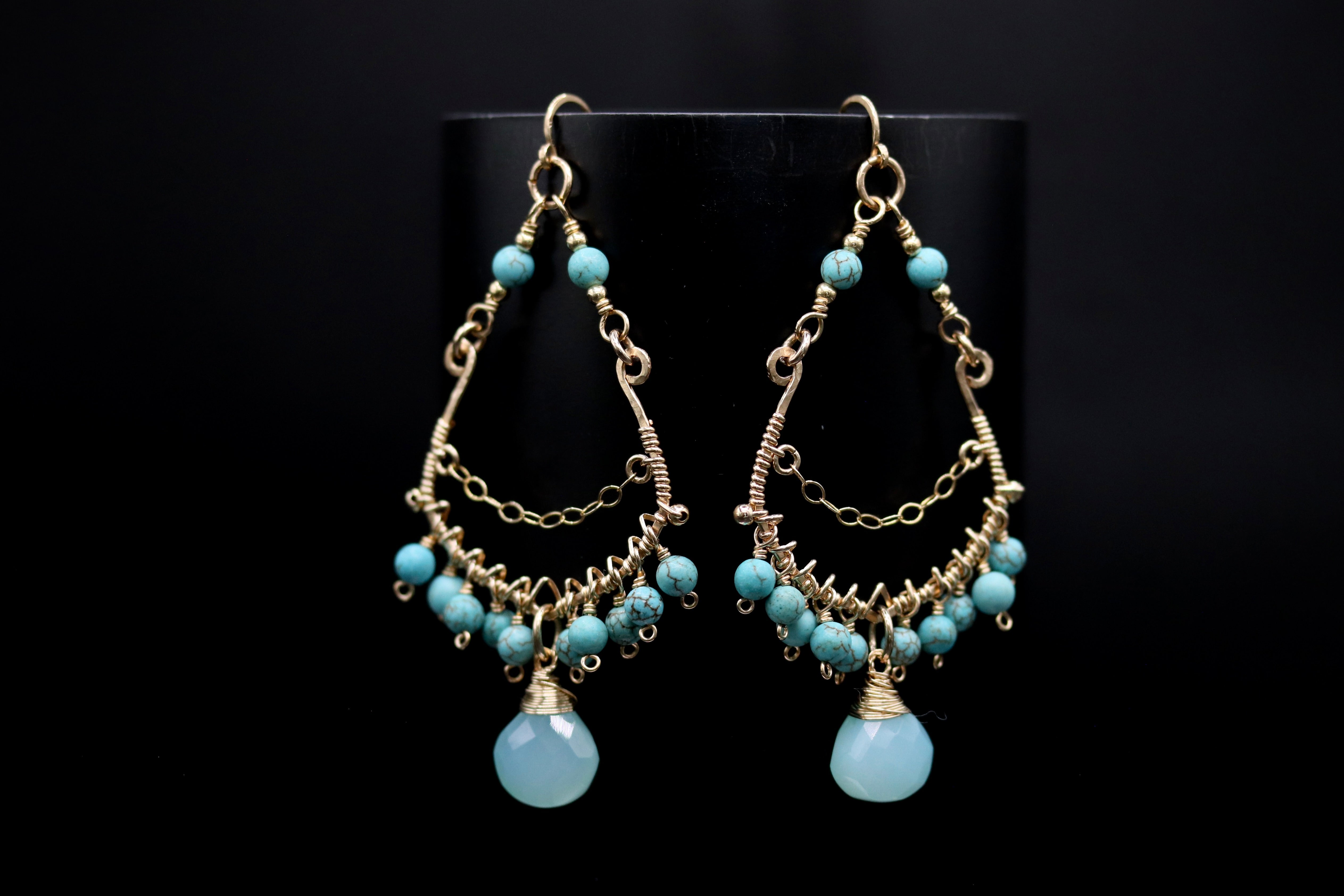 A pair of elegant earrings with turquoise stones and intricate gold metalwork, displayed against a black background.