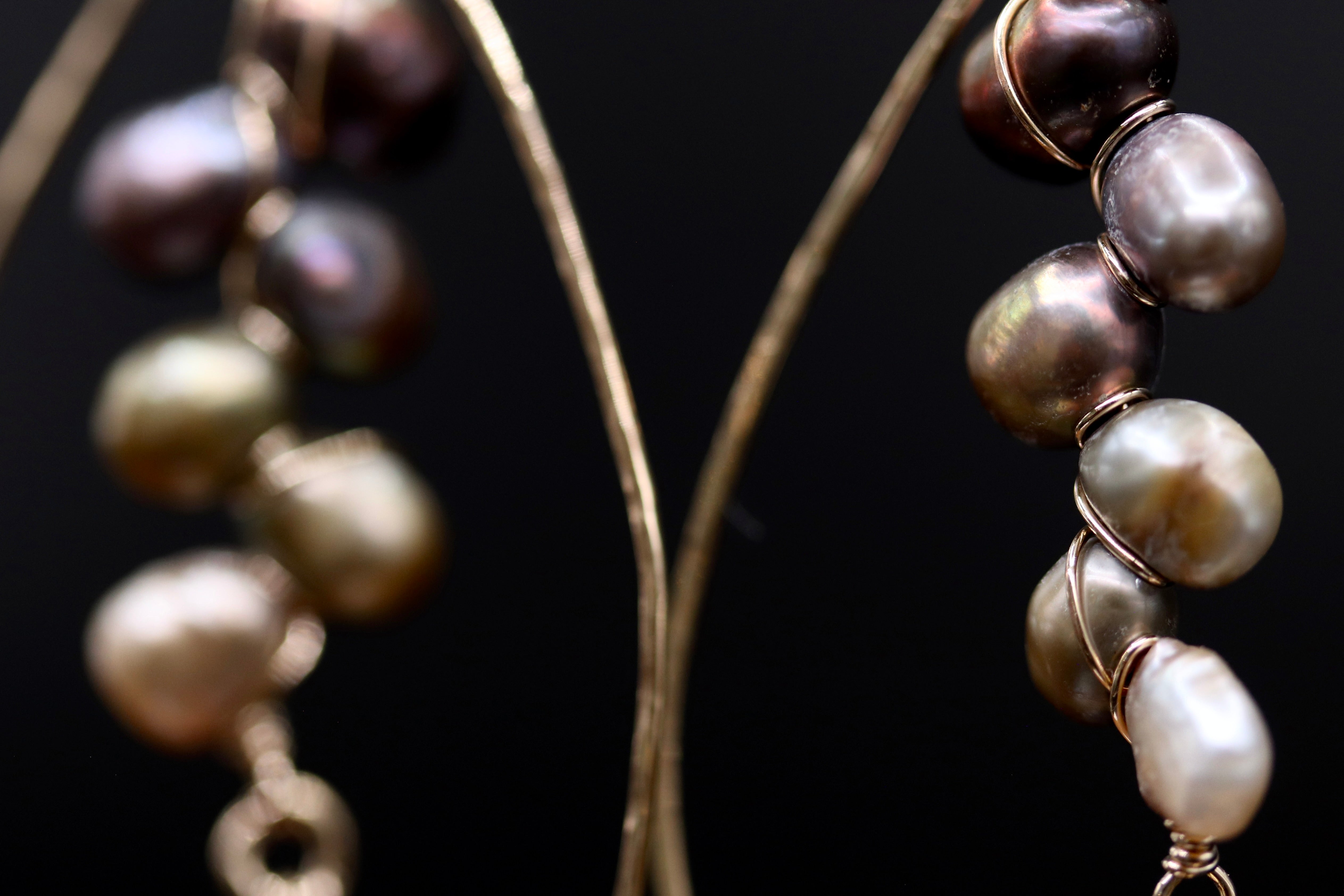 A close-up view of a pair of earrings with a combination of brown and white pearls, each adorned with a gold wire.