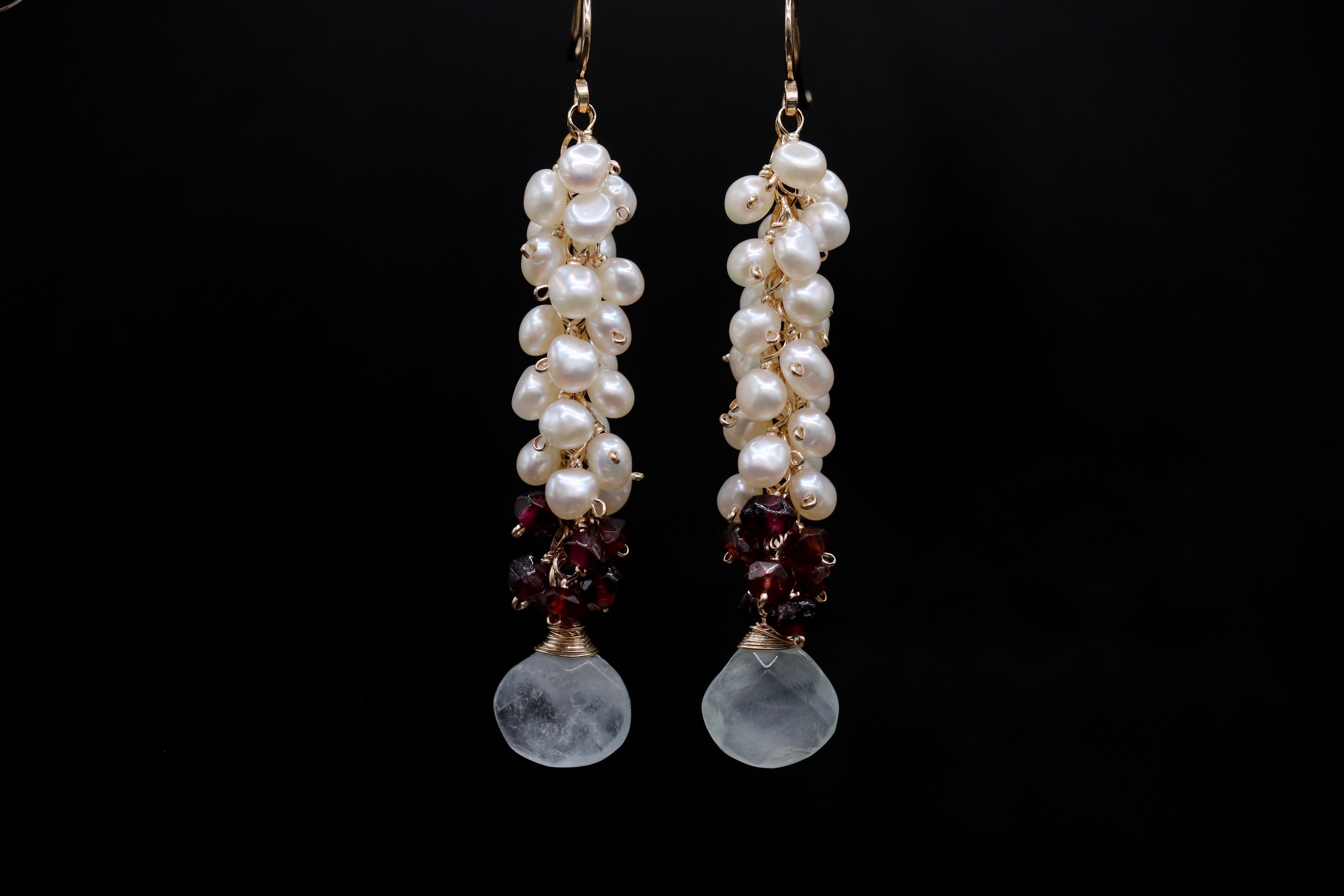 A pair of elegant earrings with white pearls and garnet stones hanging from the ends.