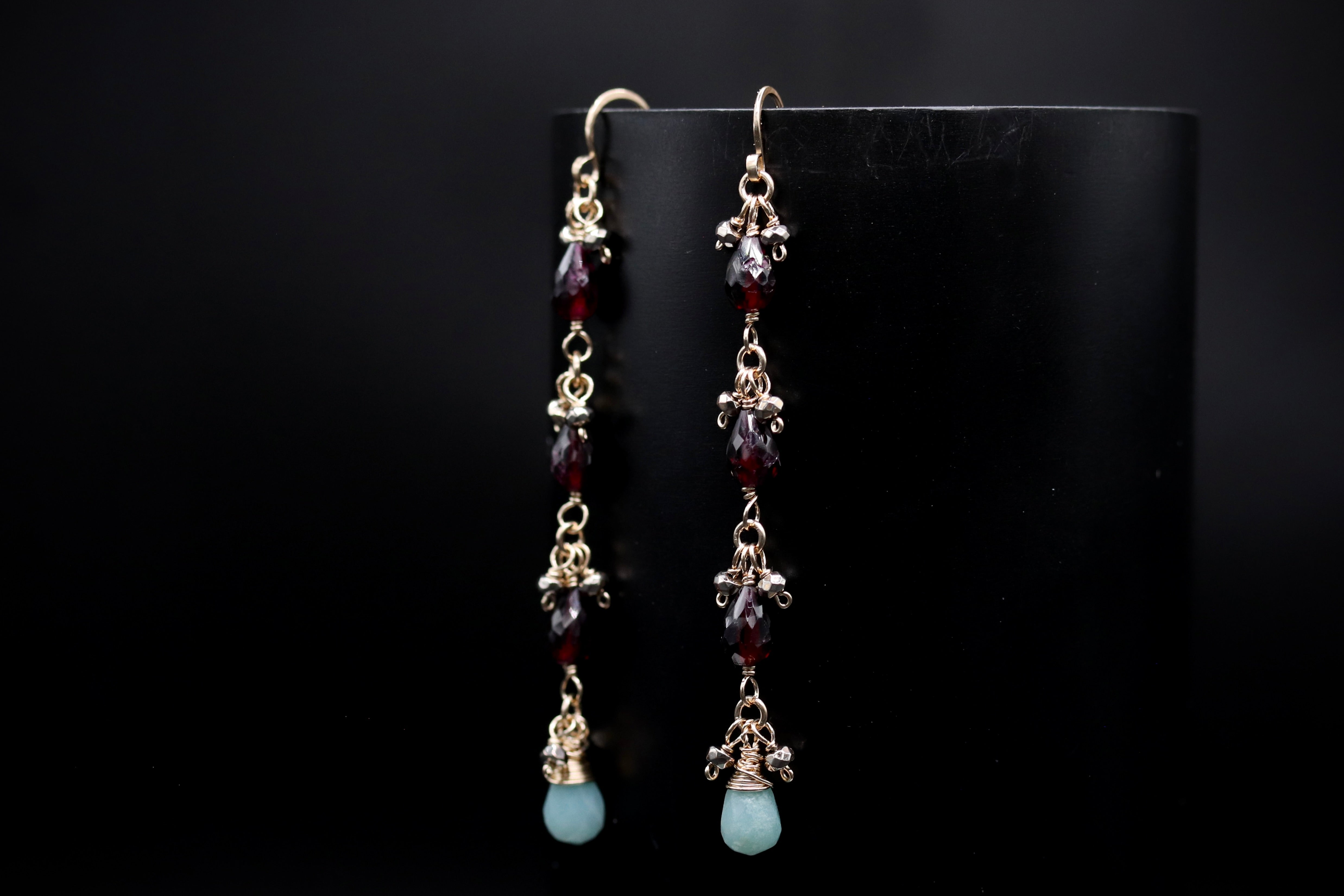 A pair of elegant earrings with a combination of red and blue gemstones, hanging from a black background.